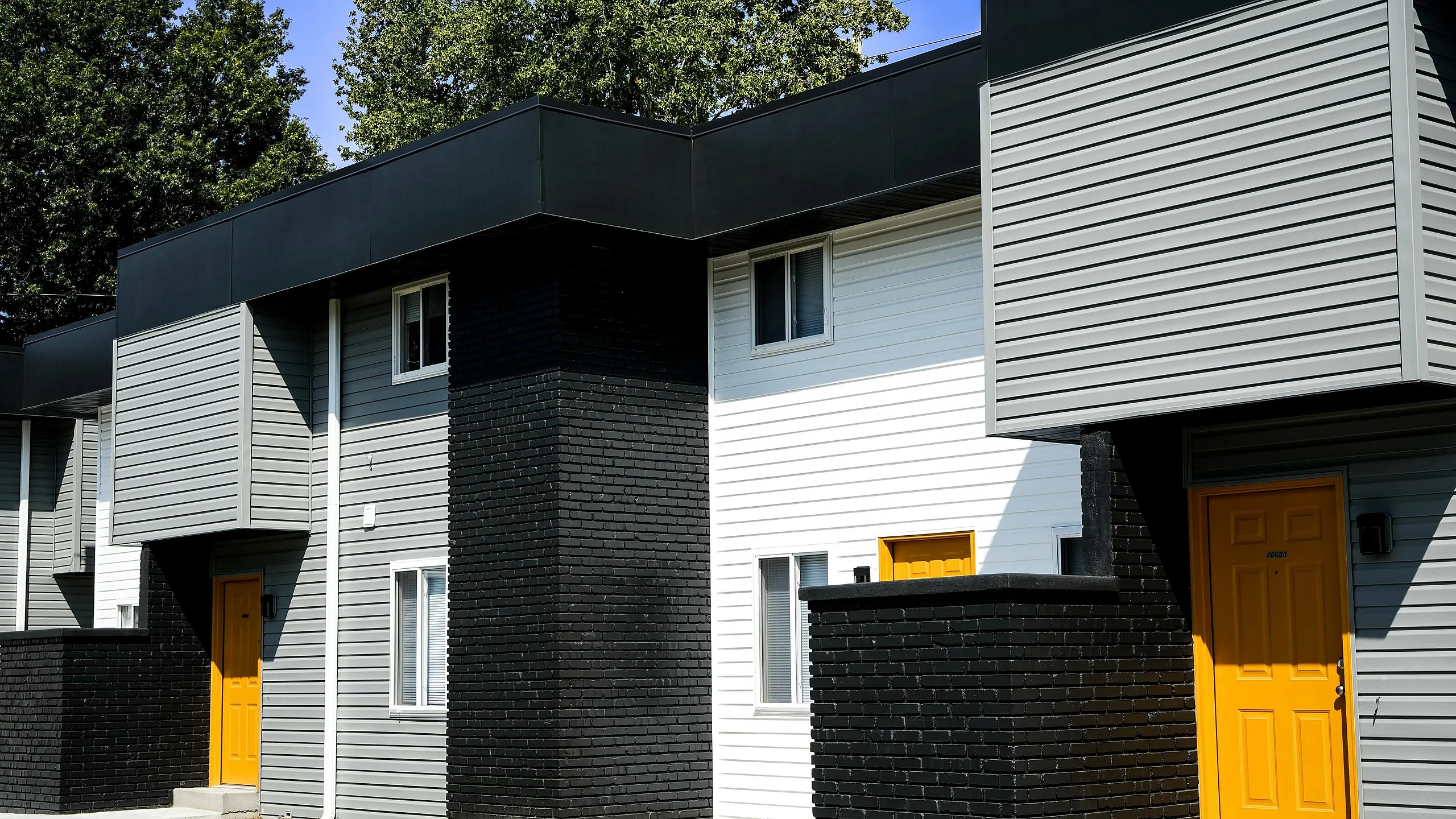 Chic modern townhouse exterior with bold yellow doors, sleek black and gray siding, and a manicured front lawn.