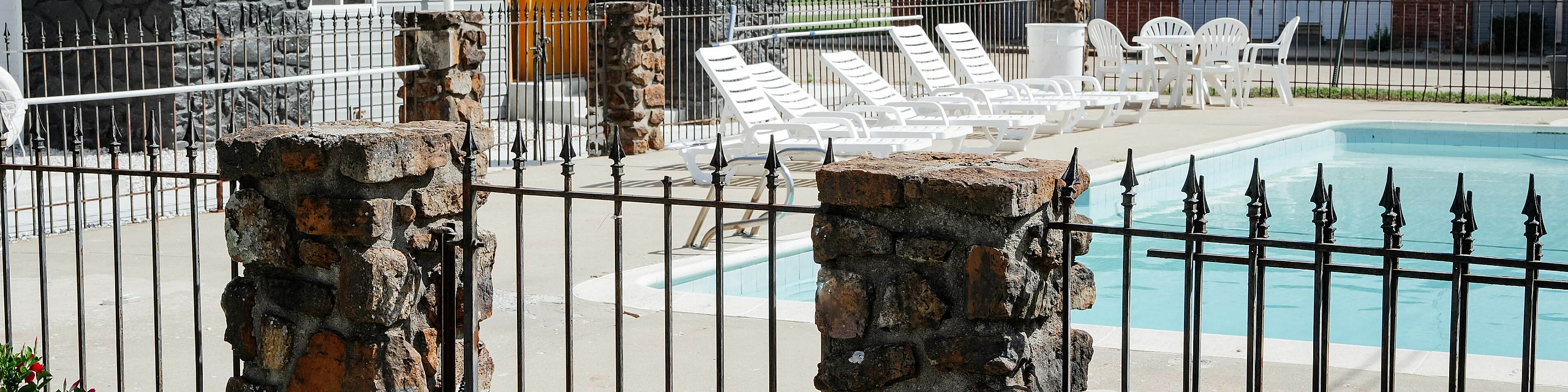 Charming residential complex featuring a serene outdoor pool area with lounge chairs, surrounded by elegant stone fencing and vibrant red flowers.