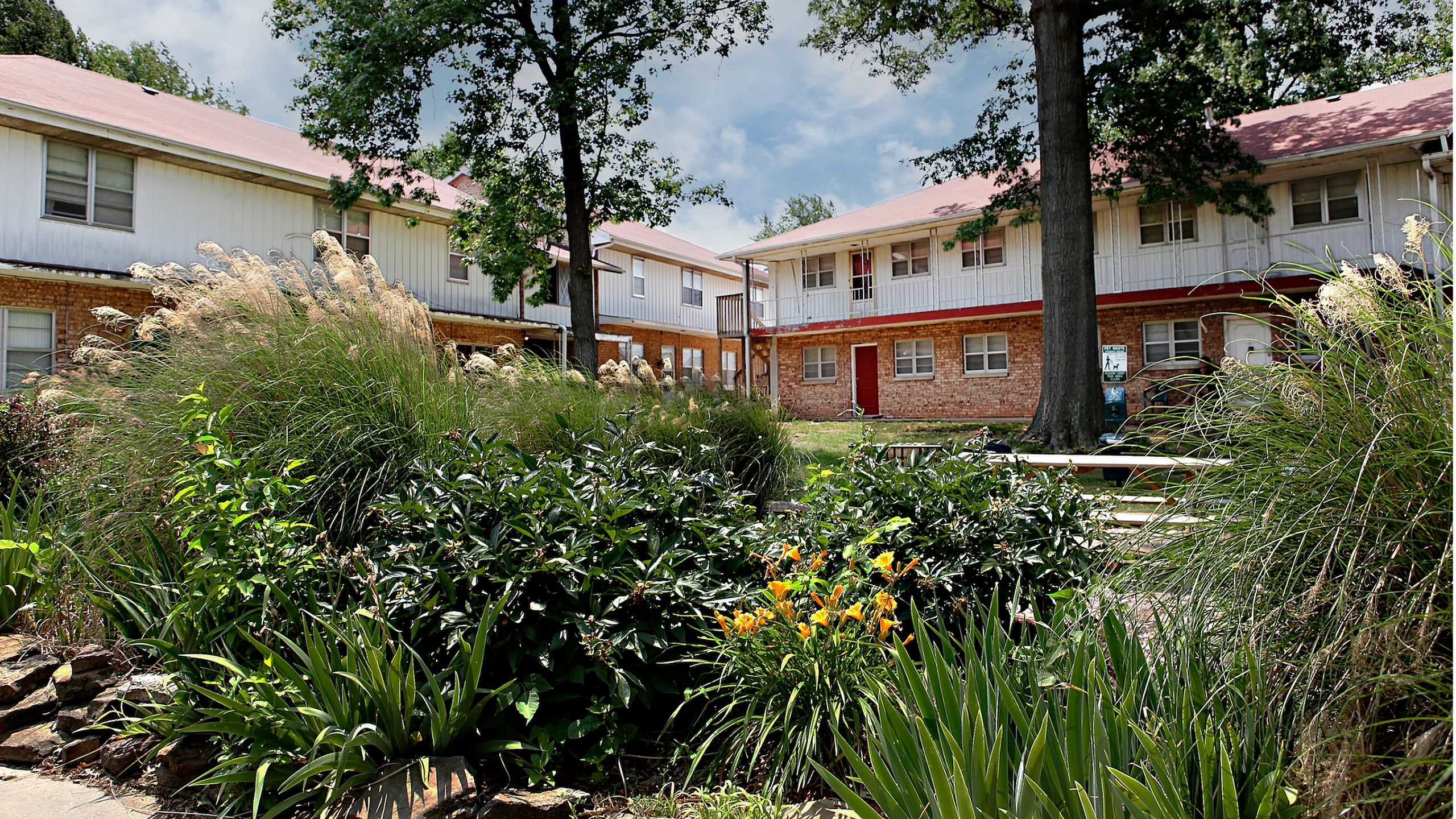 Charming apartment building surrounded by lush greenery and vibrant flowers, offering a serene living environment.