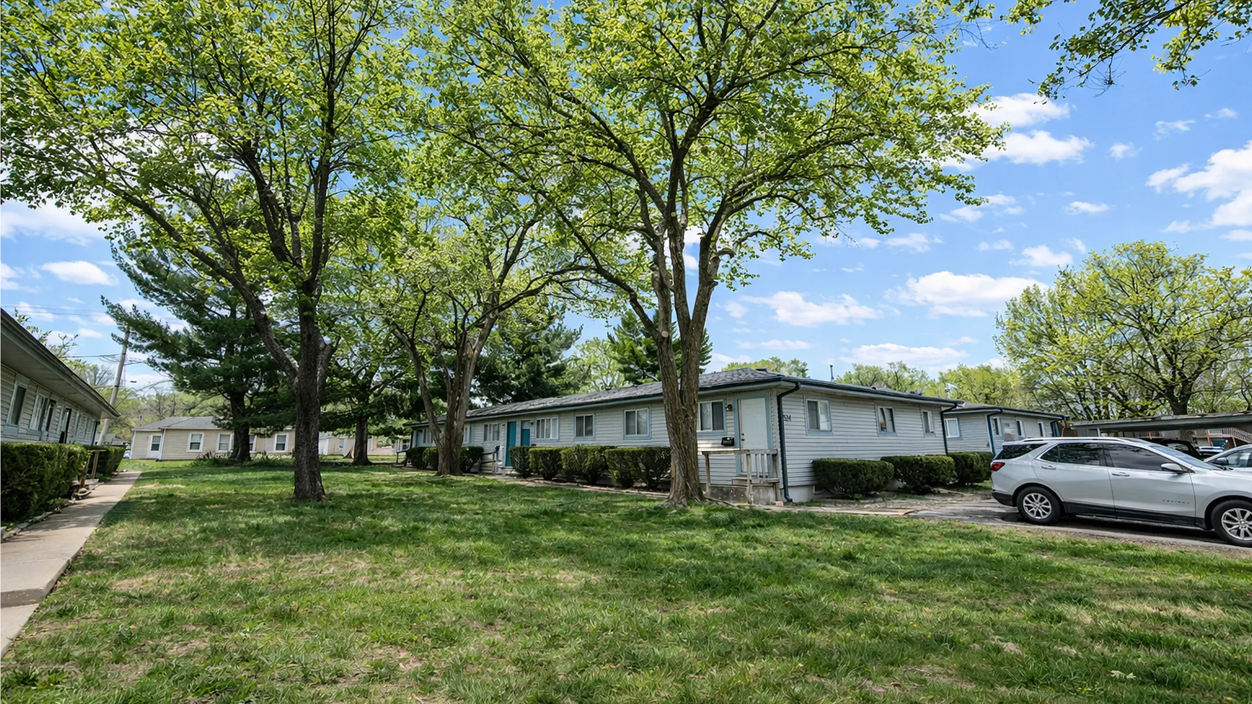 Charming residential complex surrounded by lush greenery and tall trees, offering serene outdoor space and convenient parking.