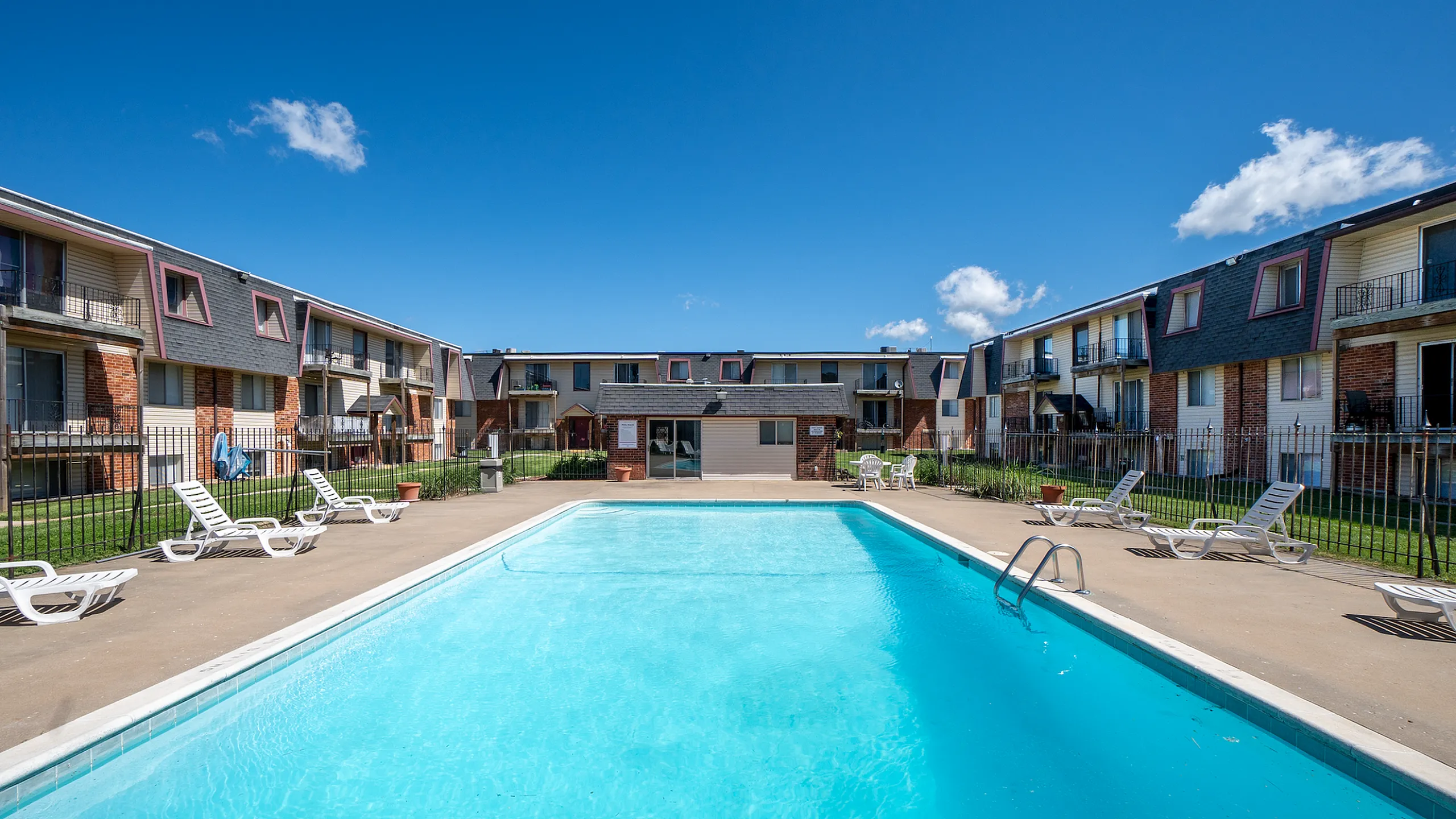 Inviting apartment complex featuring a sparkling outdoor pool and sun loungers, perfect for relaxation and leisure under a clear blue sky.