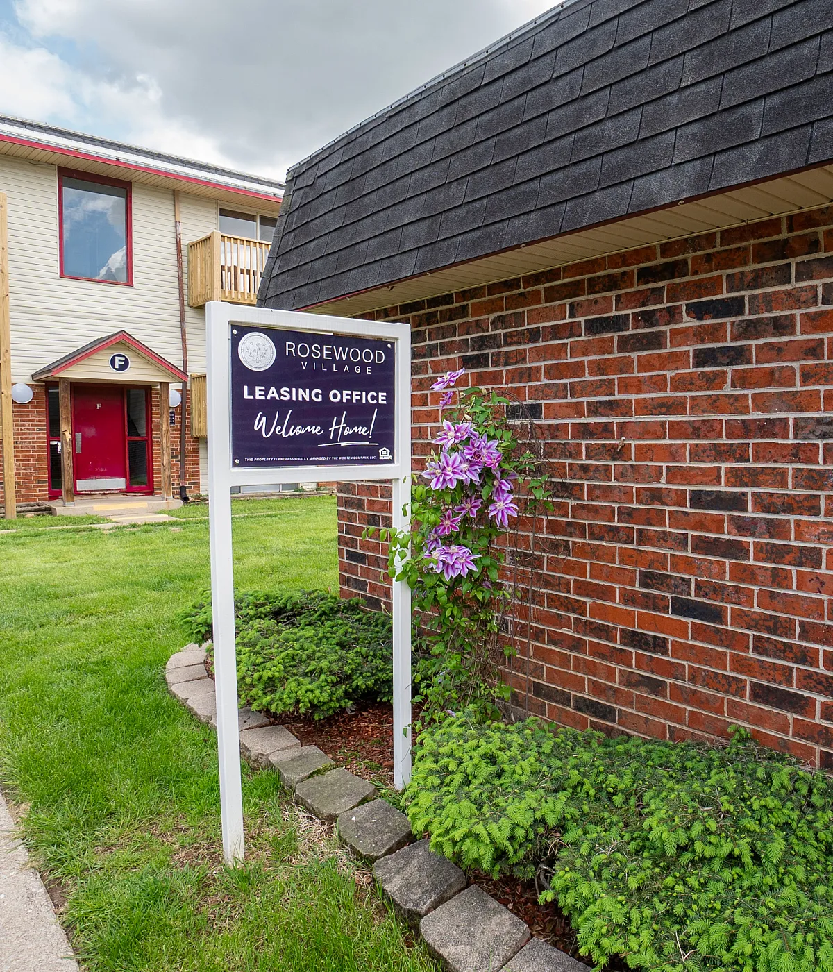 Charming Rosewood Village leasing office surrounded by vibrant flowers and lush greenery, inviting you to a welcoming community.