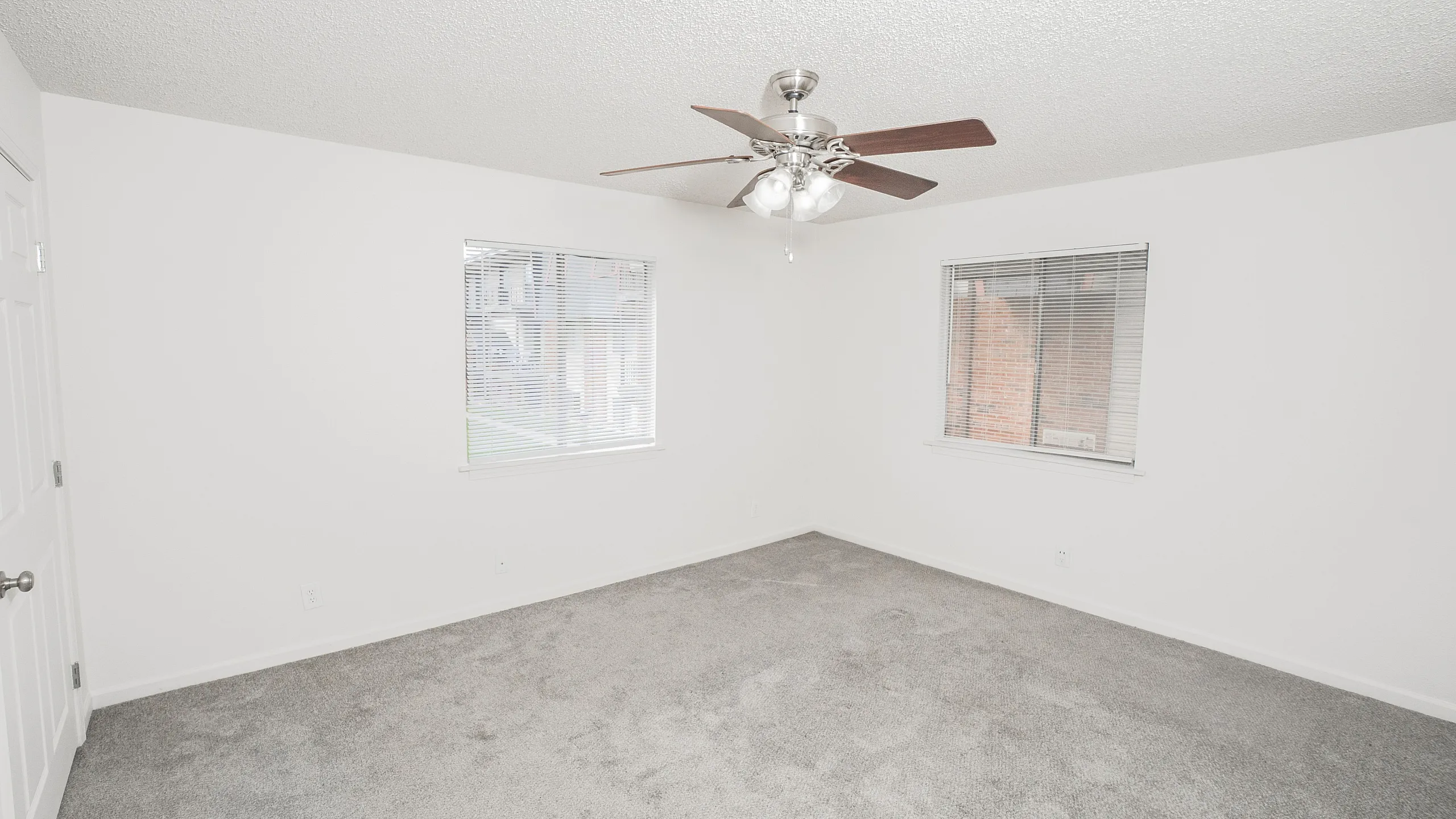 Bright and airy room with fresh carpet, white walls, ceiling fan, and large windows providing abundant natural light.