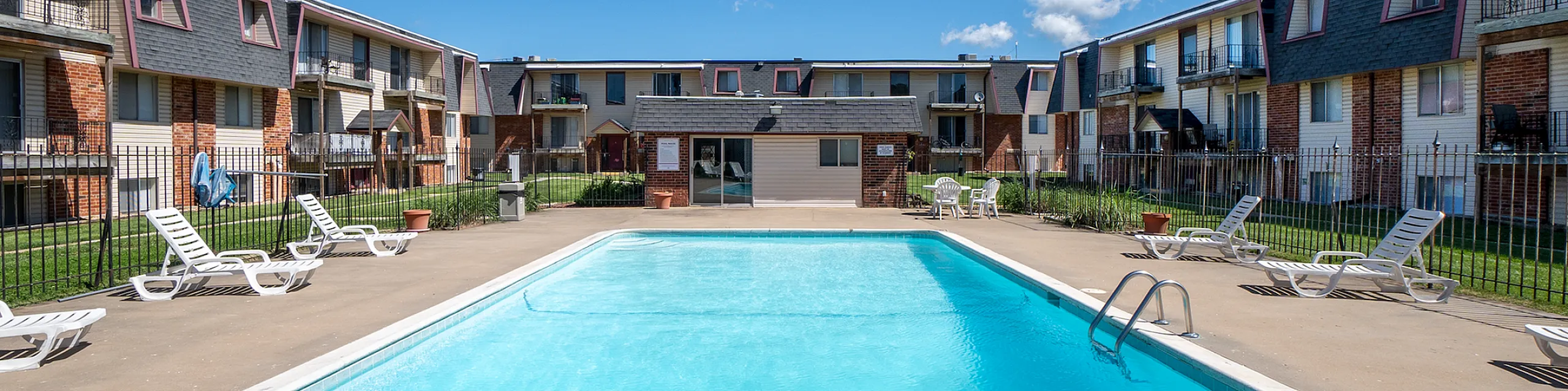 Inviting apartment complex boasting a sparkling outdoor pool surrounded by sun loungers and charming brick architecture.