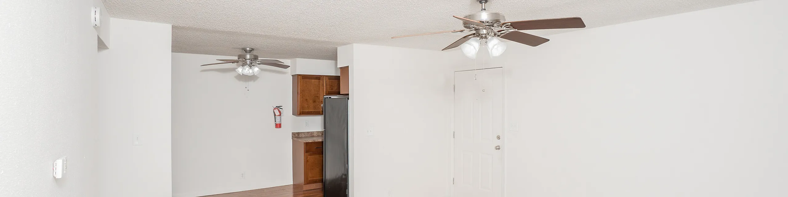 Bright and airy living space featuring elegant ceiling fans, plush carpeting, and a conveniently placed kitchen area with modern appliances.