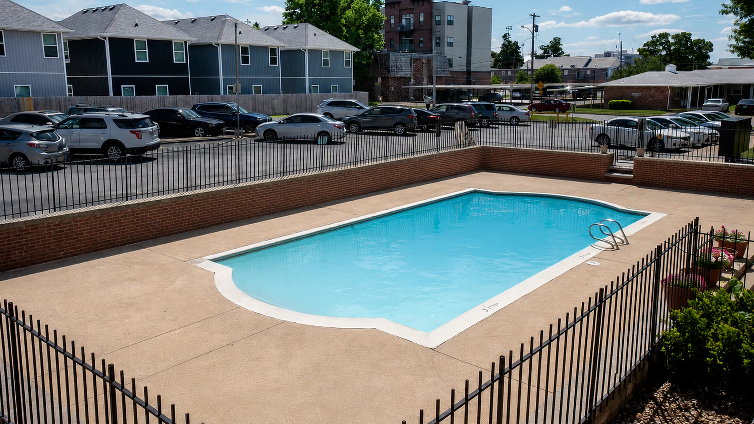 Inviting outdoor pool area surrounded by a secure fence, with vibrant greenery and ample parking in a suburban setting.