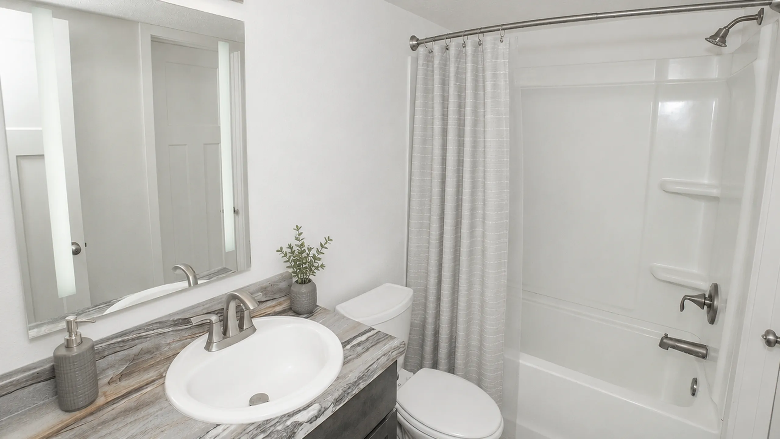 Contemporary bathroom with elegant lighting, a sleek vanity, and a bathtub with a soft gray shower curtain.
