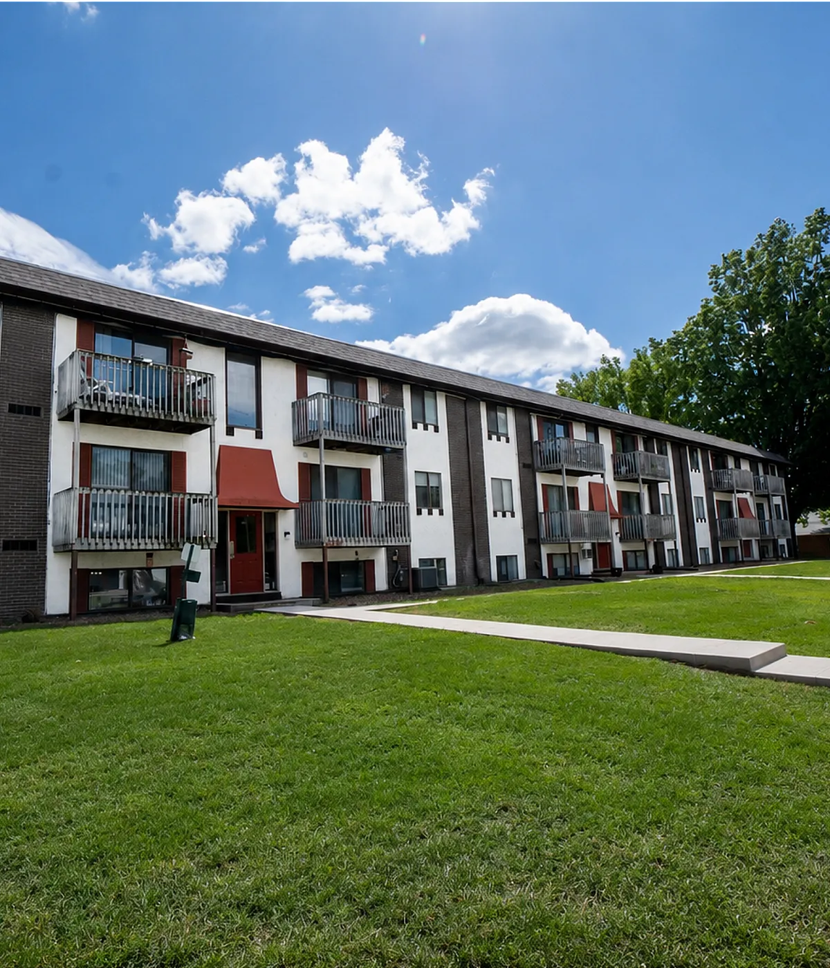 Charming three-story apartment complex with private balconies and lush green lawns, perfect for modern living.