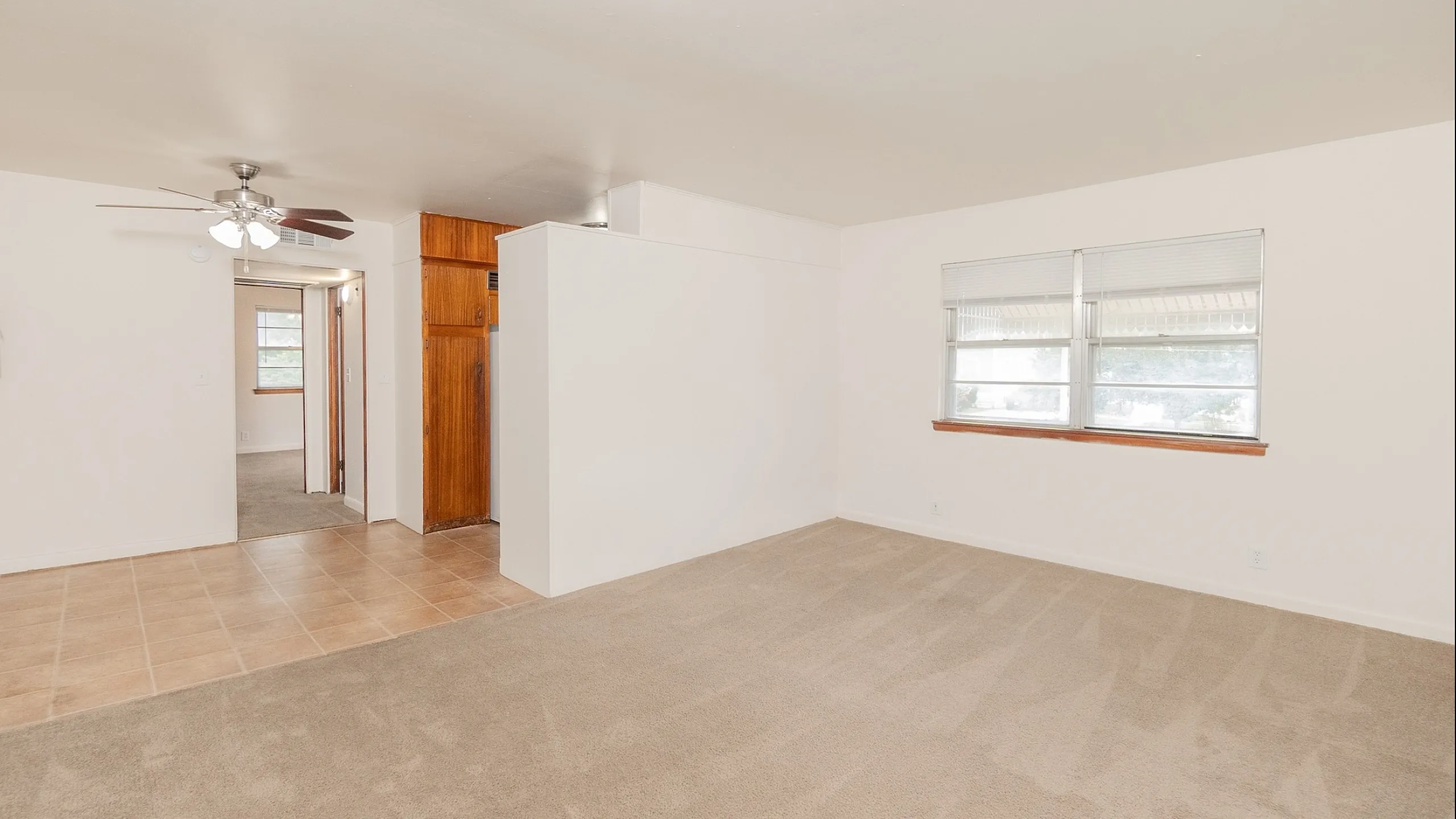 Bright open-concept living area featuring large windows and a spacious layout, seamlessly connecting to a cozy hallway.