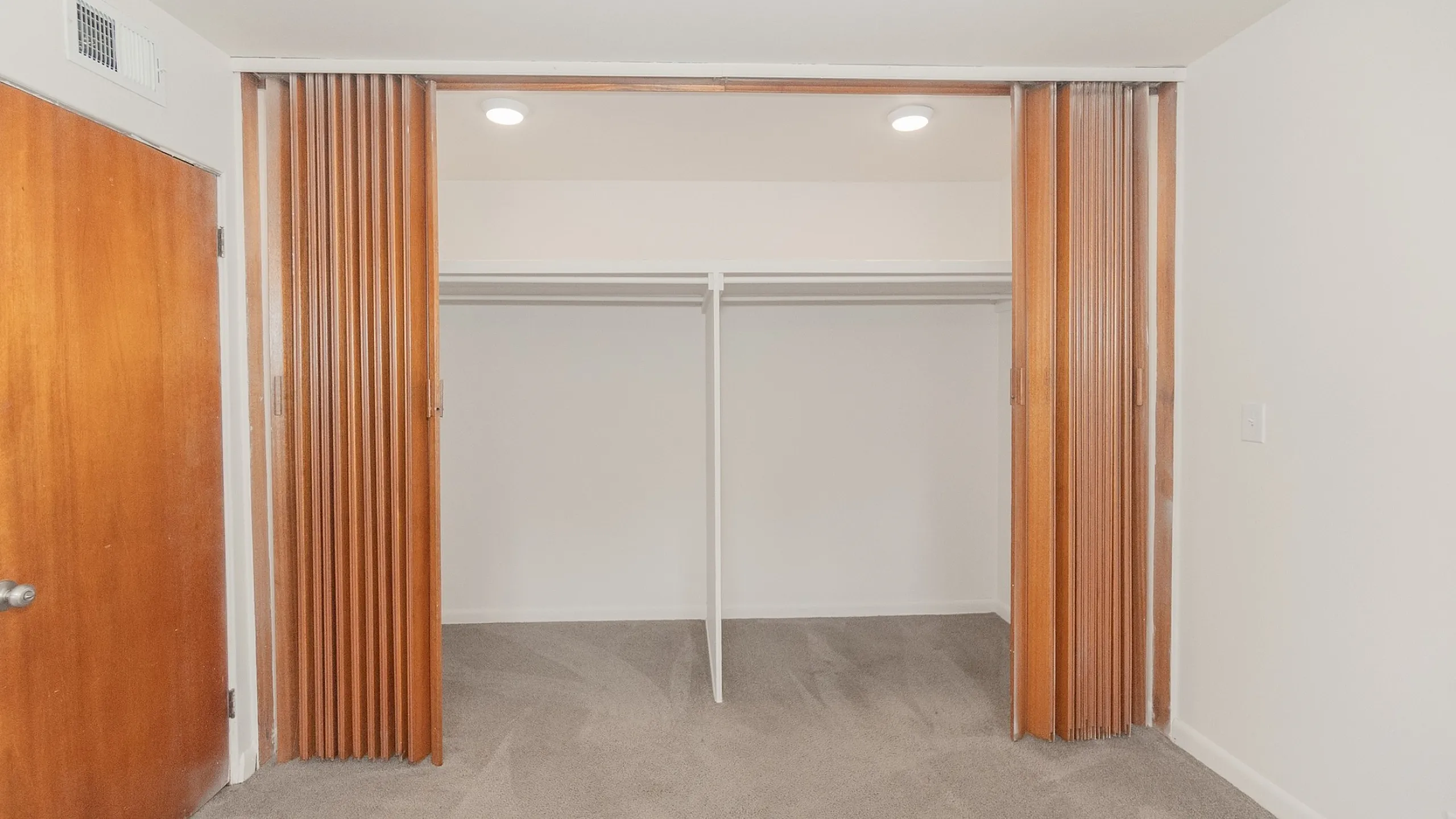 Spacious walk-in closet with sleek sliding wooden doors and plush carpet flooring, perfect for organized living.