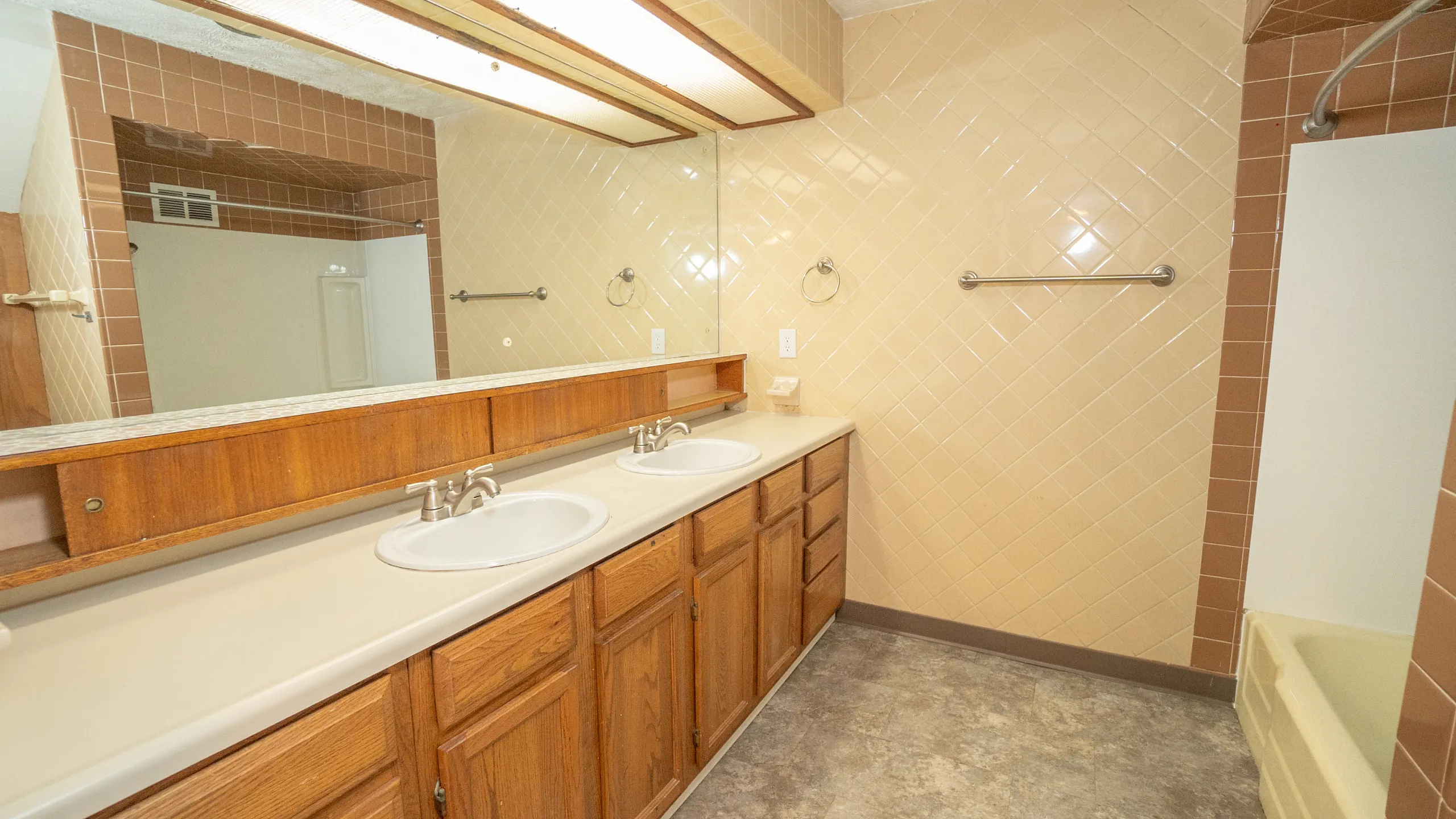 Spacious bathroom featuring dual sinks, elegant wooden cabinetry, and stylish tiled walls, offering modern comfort and convenience.
