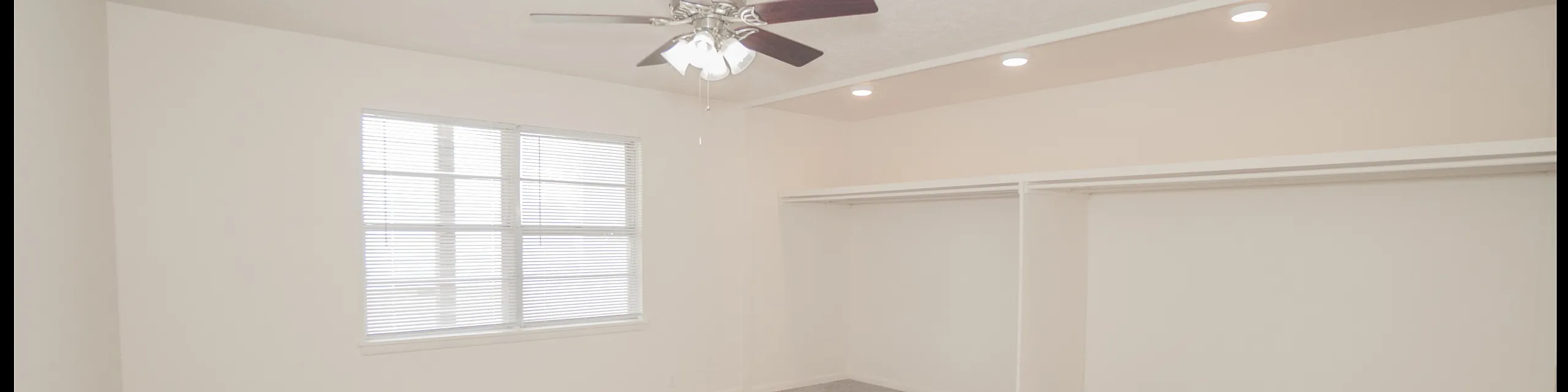 Spacious bedroom with plush carpet, large window, and ceiling fan in a modern apartment.
