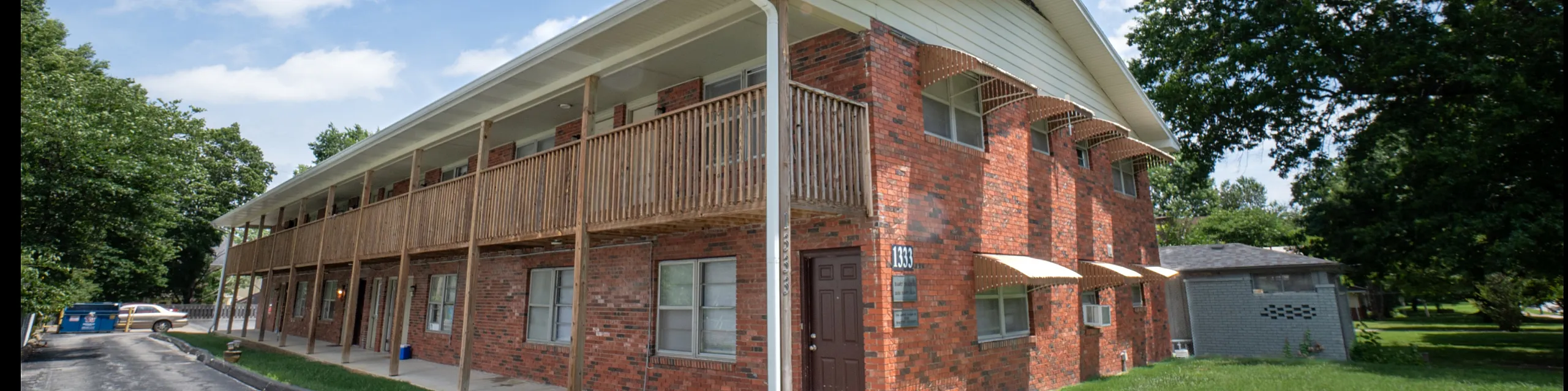 Charming red brick apartment building with wooden railings and lush greenery, offering a cozy and inviting living environment.