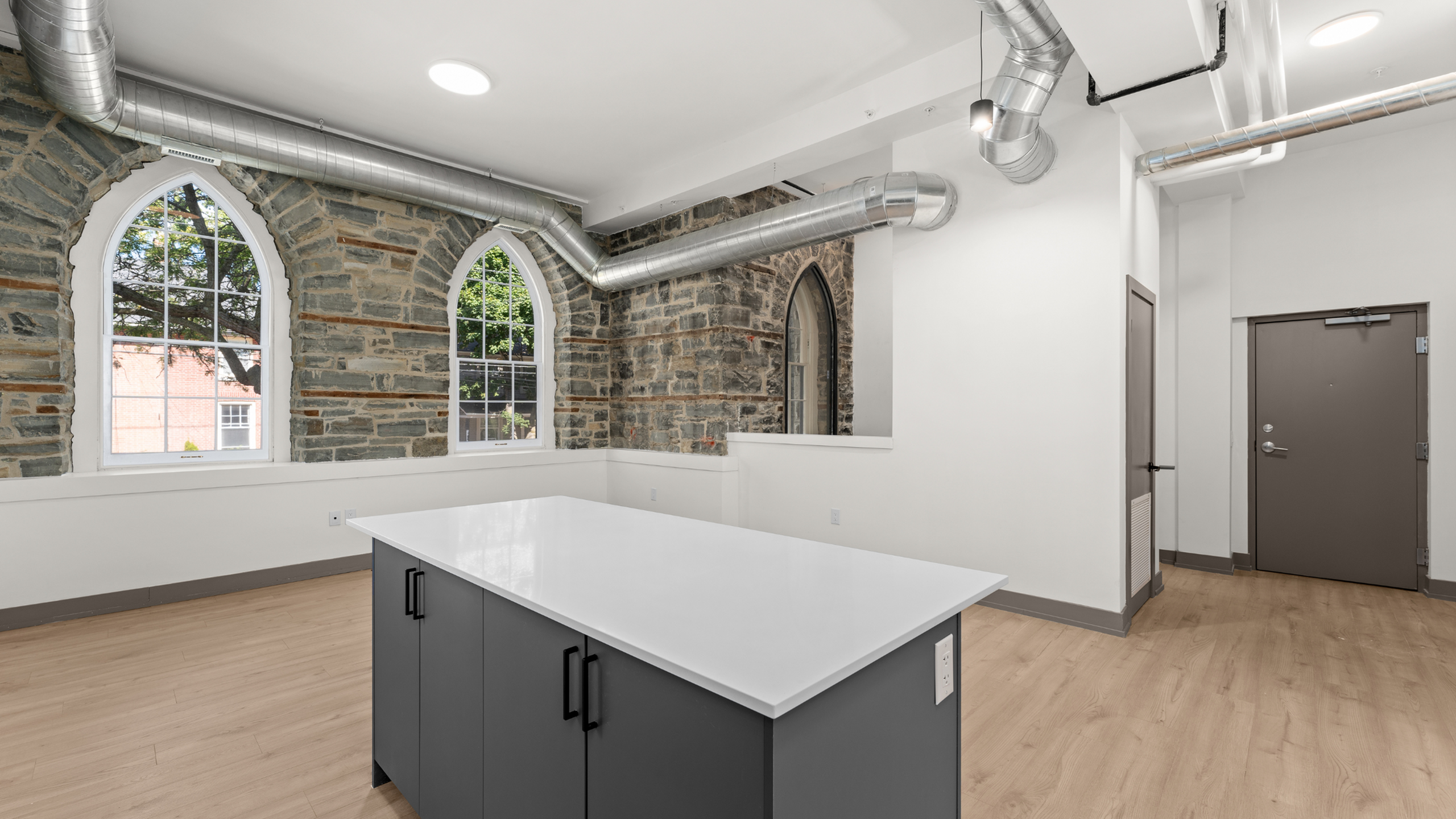 Modern loft-style apartment with exposed brick, arched windows, and sleek kitchen island.