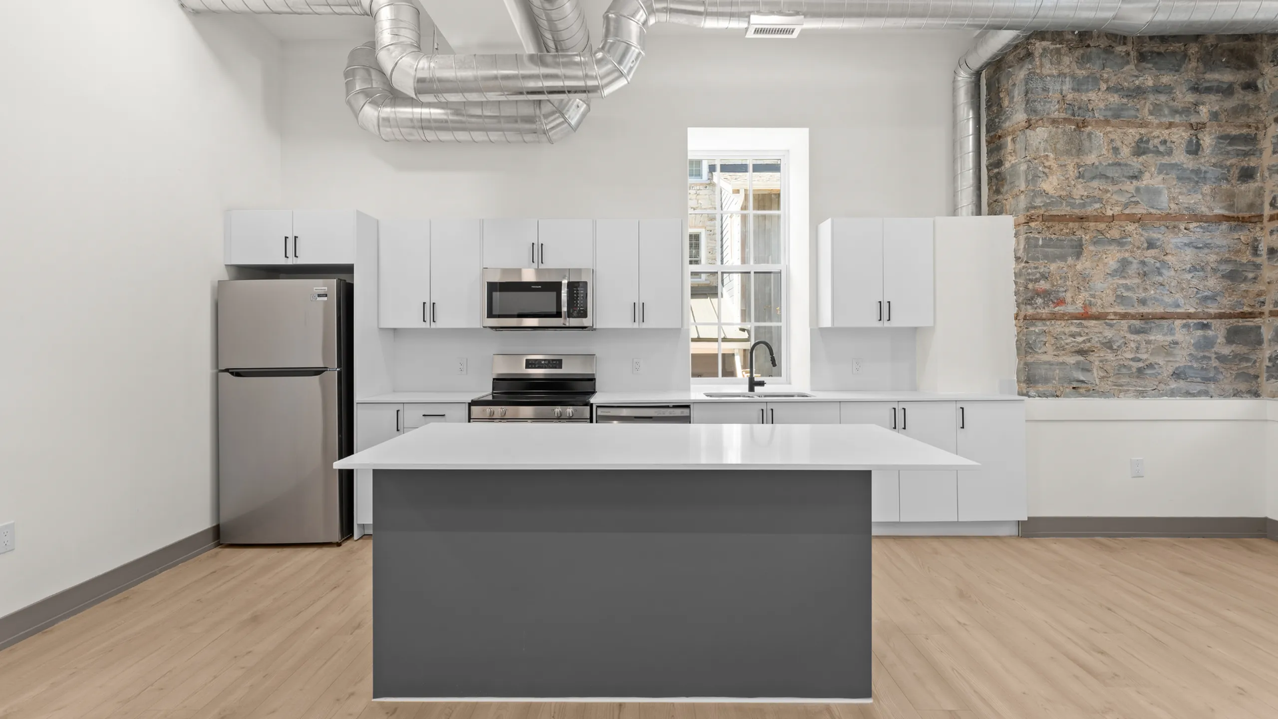 Modern kitchen with sleek stainless steel appliances, white cabinetry, and exposed ductwork, featuring a large center island and rustic stone accents.
