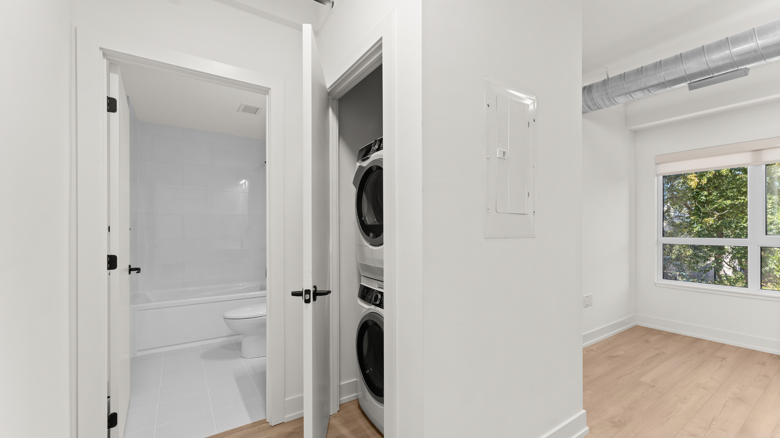 Modern apartment interior featuring a sleek in-unit washer and dryer with a bright bathroom, complemented by large windows for natural light.