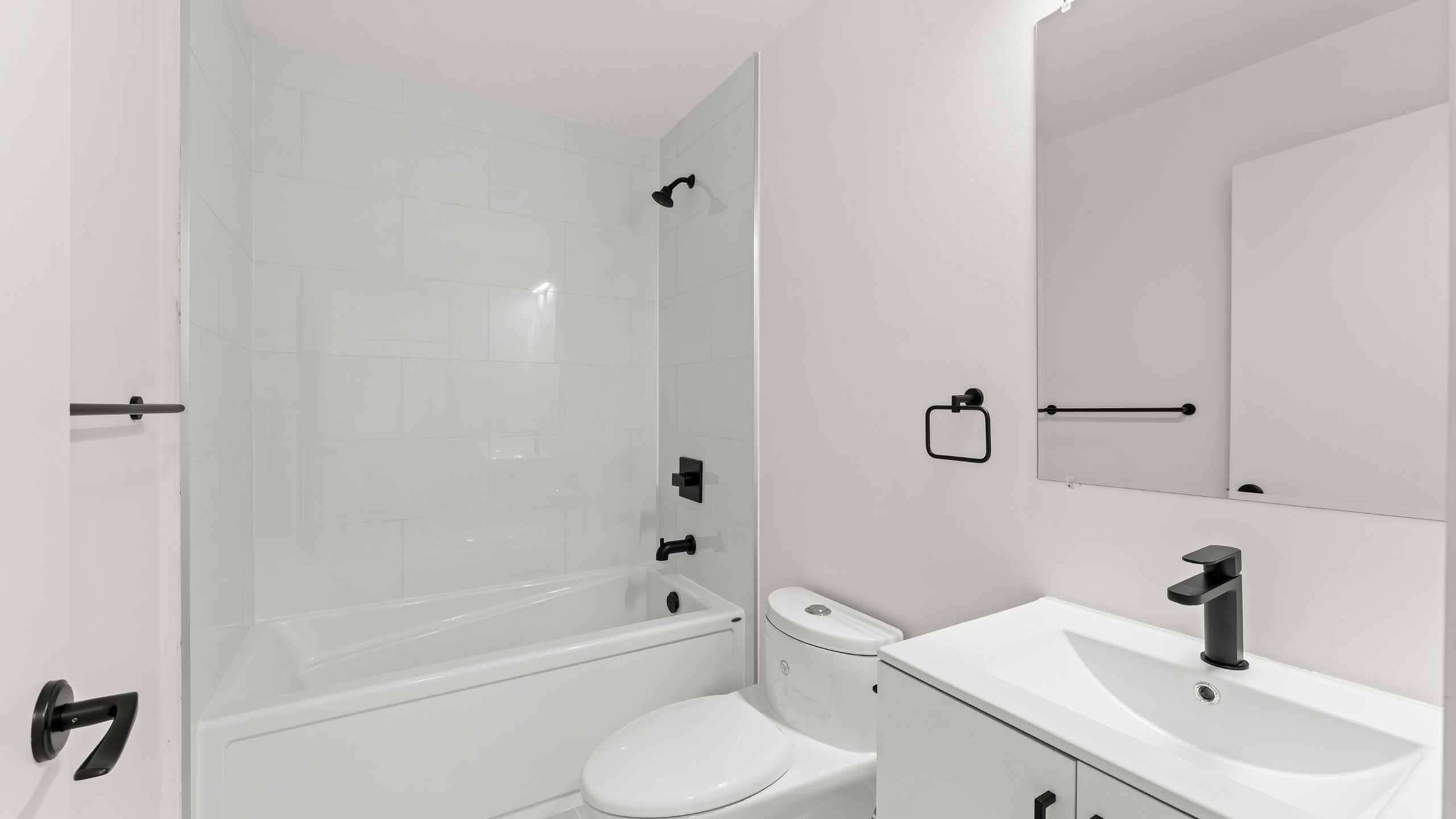 Elegant, modern bathroom featuring sleek white tiles, a luxurious bathtub, and stylish black fixtures.