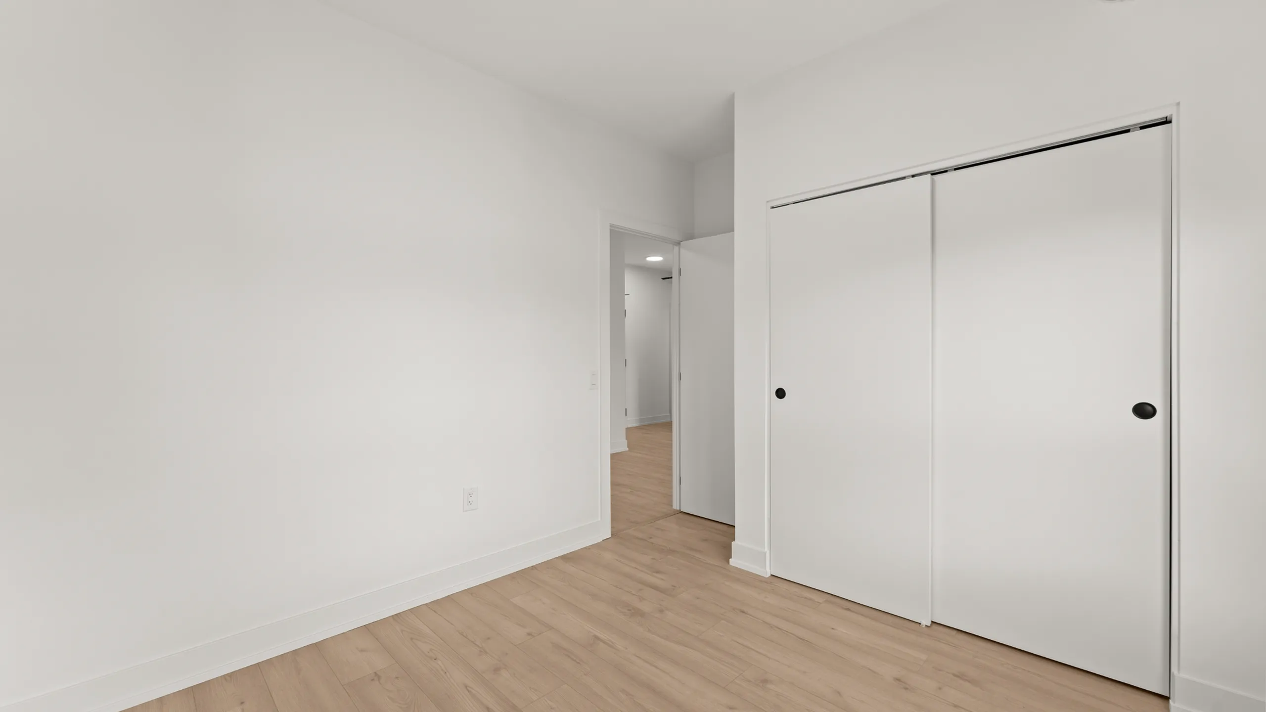 Bright, minimalist room featuring sleek wooden flooring, smooth white walls, and elegant sliding closet doors.