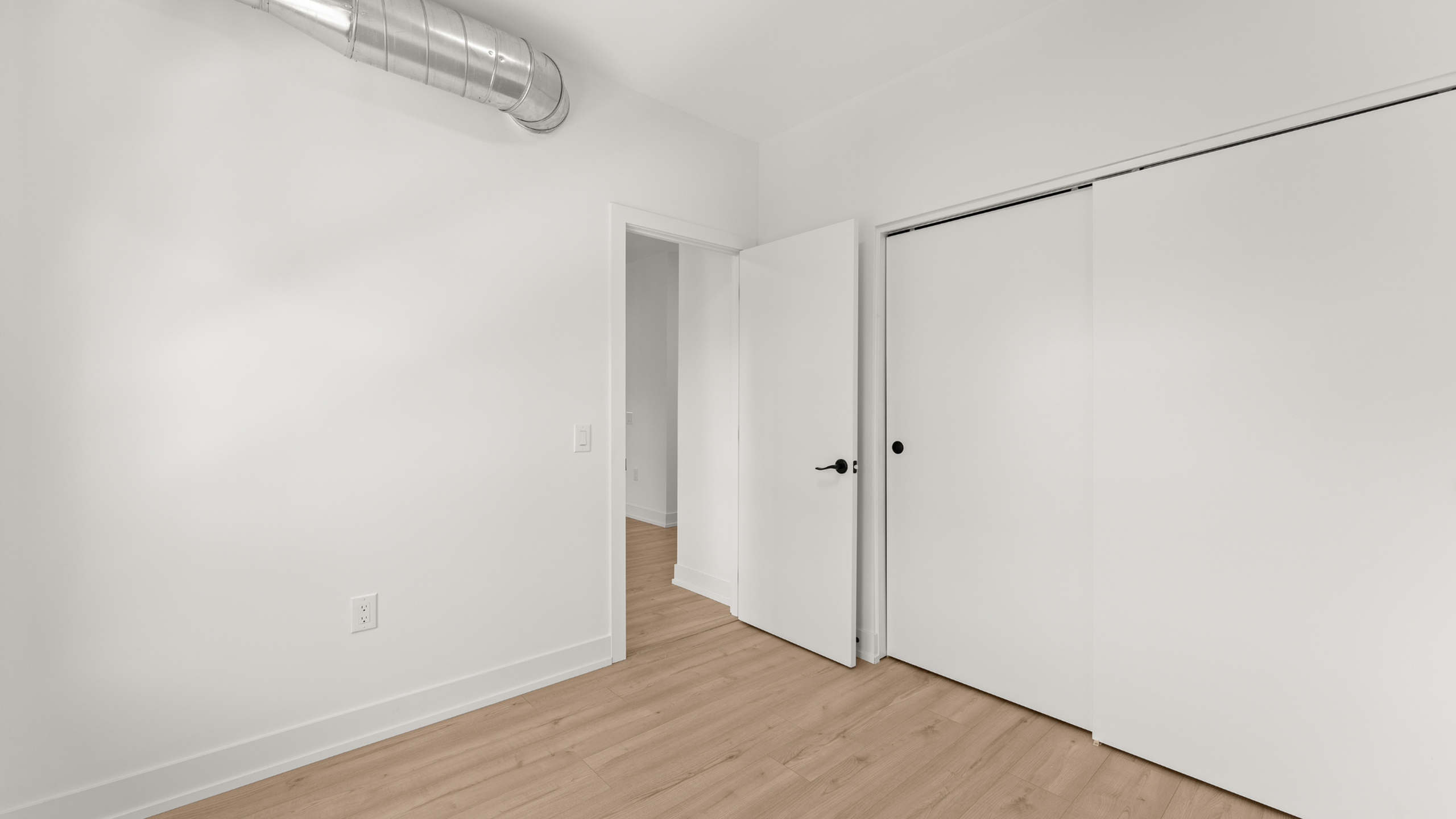 Modern white interior room with sleek wooden floors and minimalist design features a duct for a stylish industrial touch.