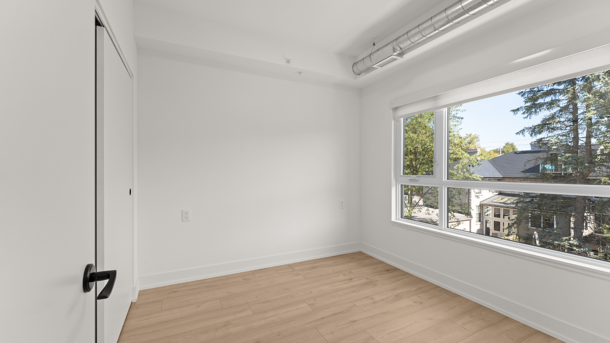 Sunlit room with stylish hardwood floors, large window offering scenic views, and sleek modern finishes.