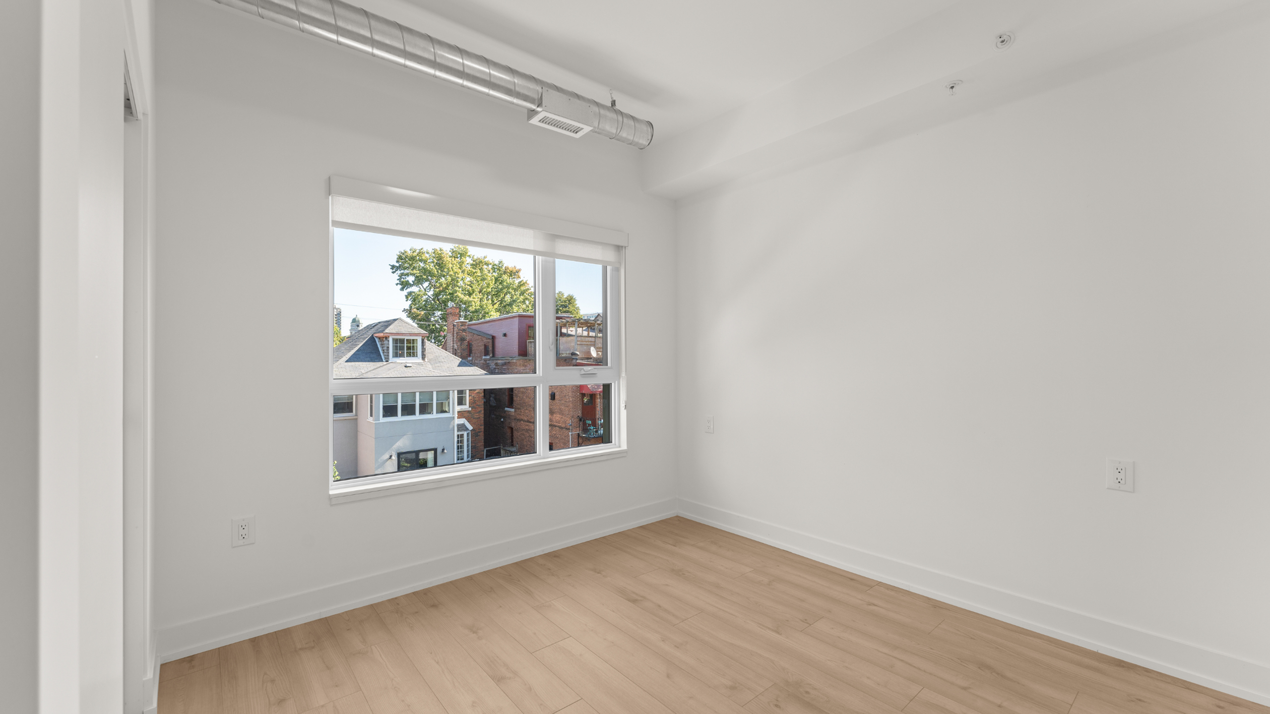 Bright, spacious room with large window providing natural light and scenic views, featuring modern finishes and wood flooring.