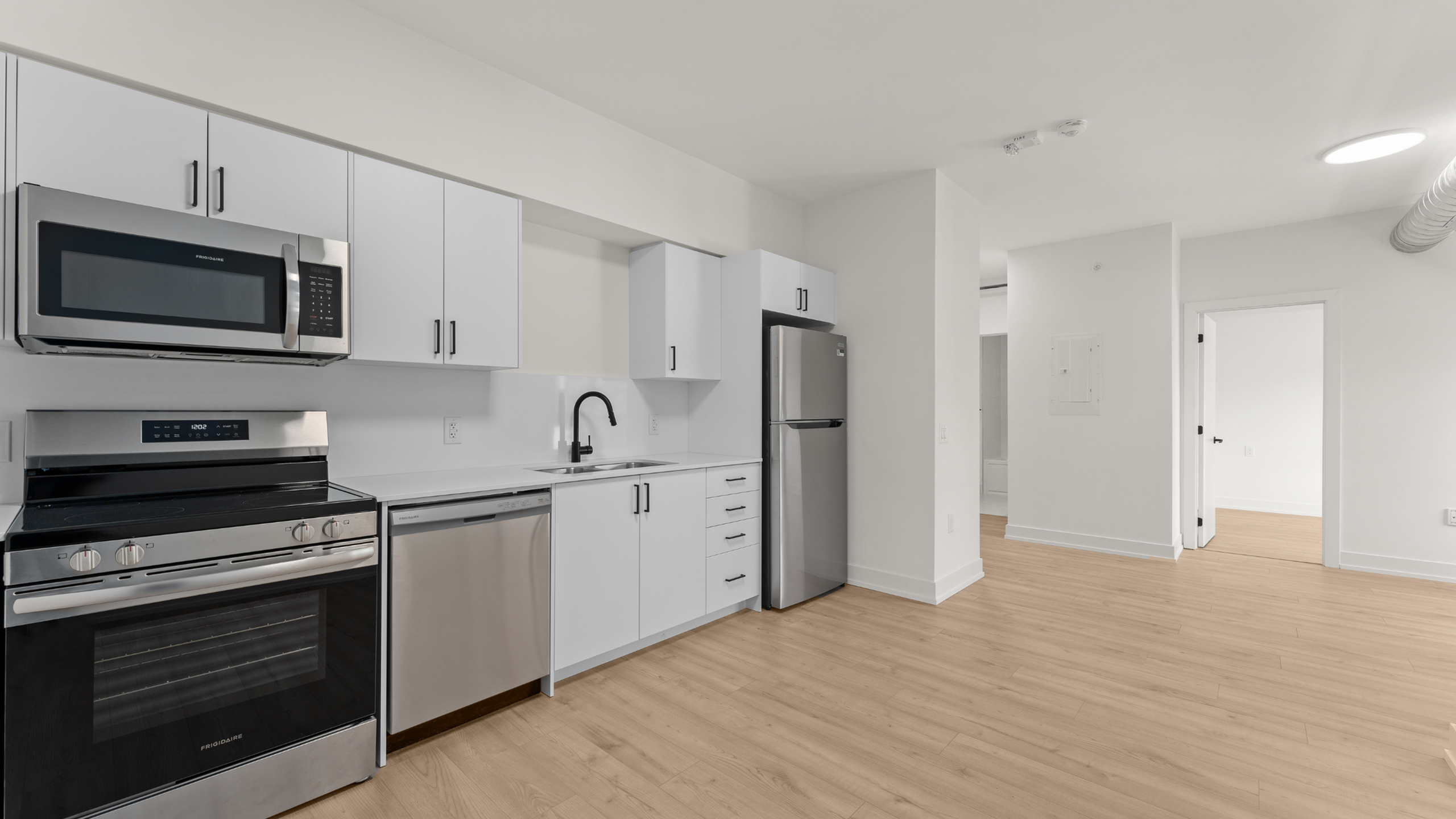 Sleek modern kitchen with stainless steel appliances, bright white cabinetry, and elegant wood flooring.