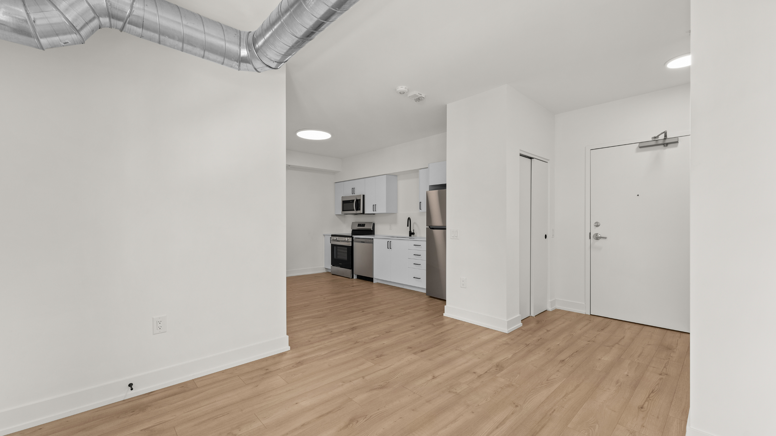 Modern apartment interior featuring sleek stainless steel appliances, light hardwood floors, and industrial exposed ductwork, offering a stylish and airy living space.