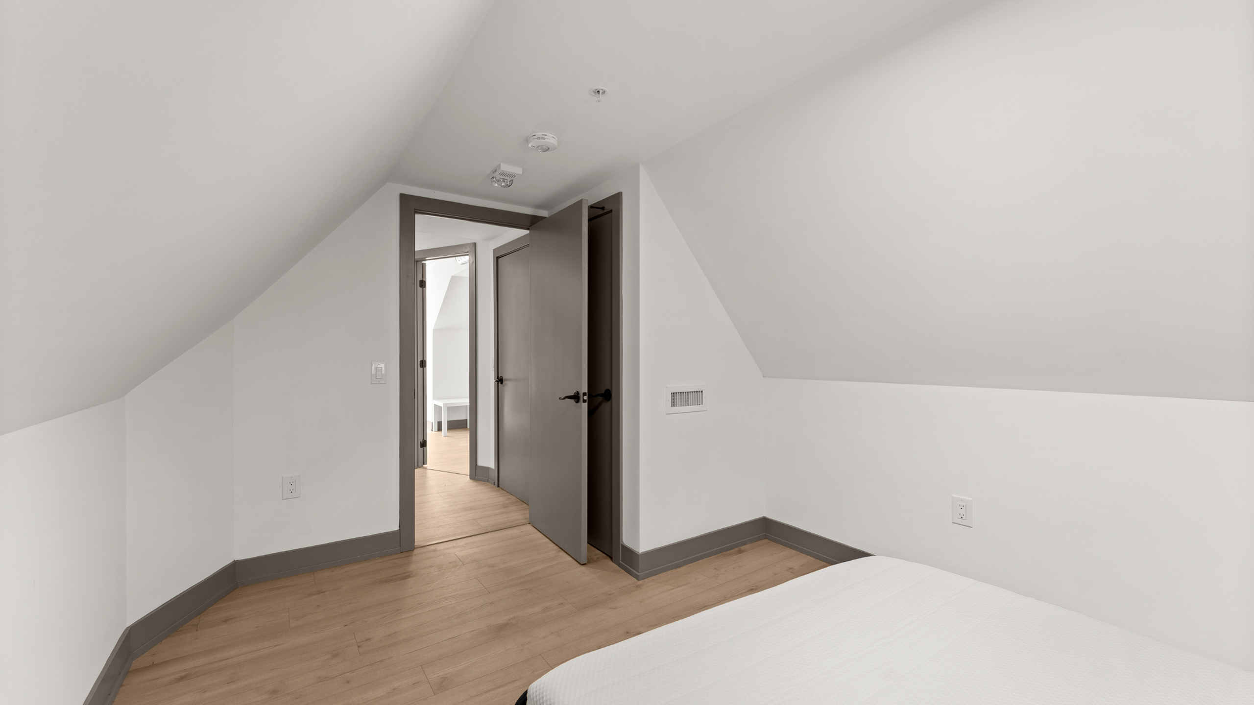 Cozy attic bedroom with sloped ceiling, warm wooden flooring, and a minimalist design.