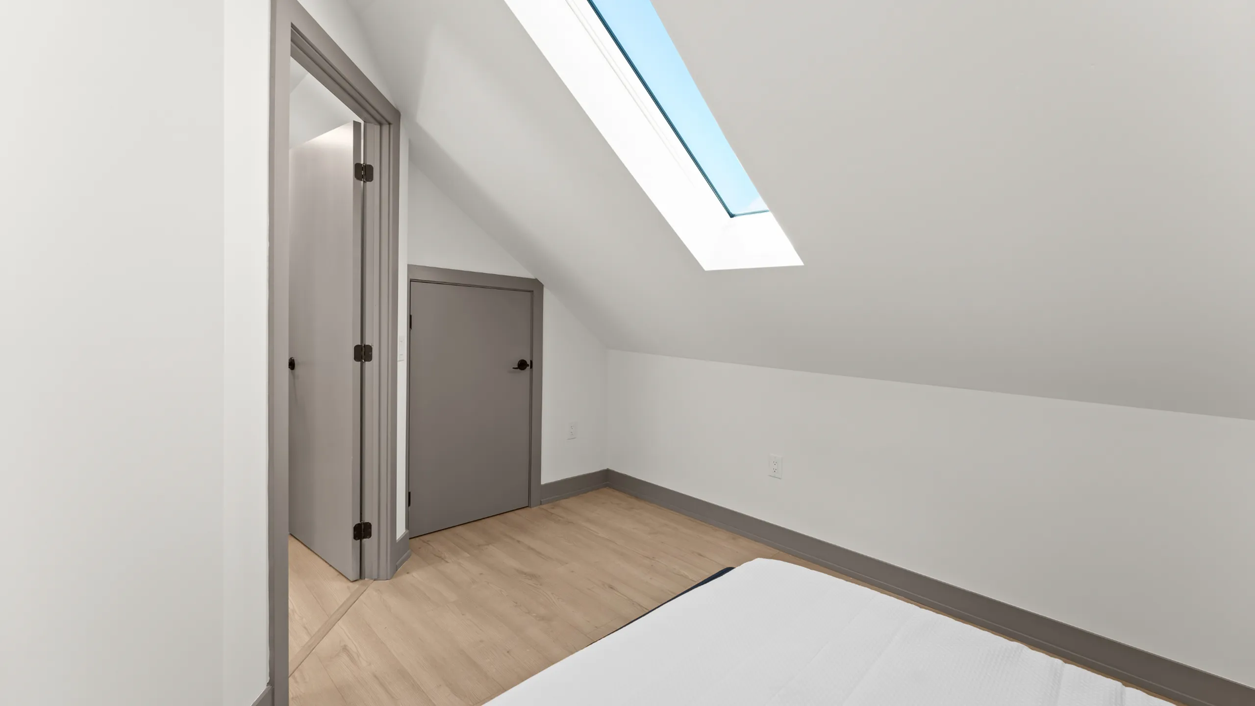 Charming attic bedroom with a skylight illuminating the space, featuring warm wooden flooring and a modern aesthetic.