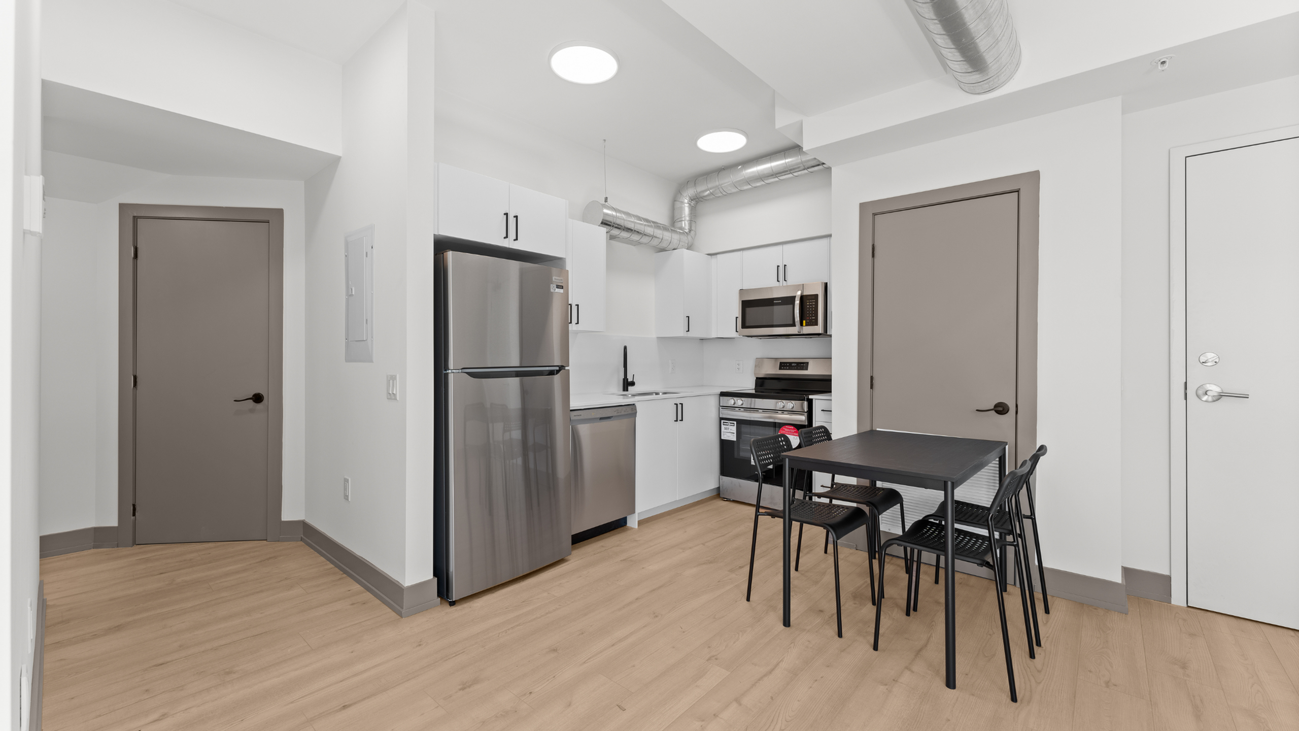 Modern kitchen with stainless steel appliances, sleek cabinetry, and a cozy dining area under stylish ductwork.