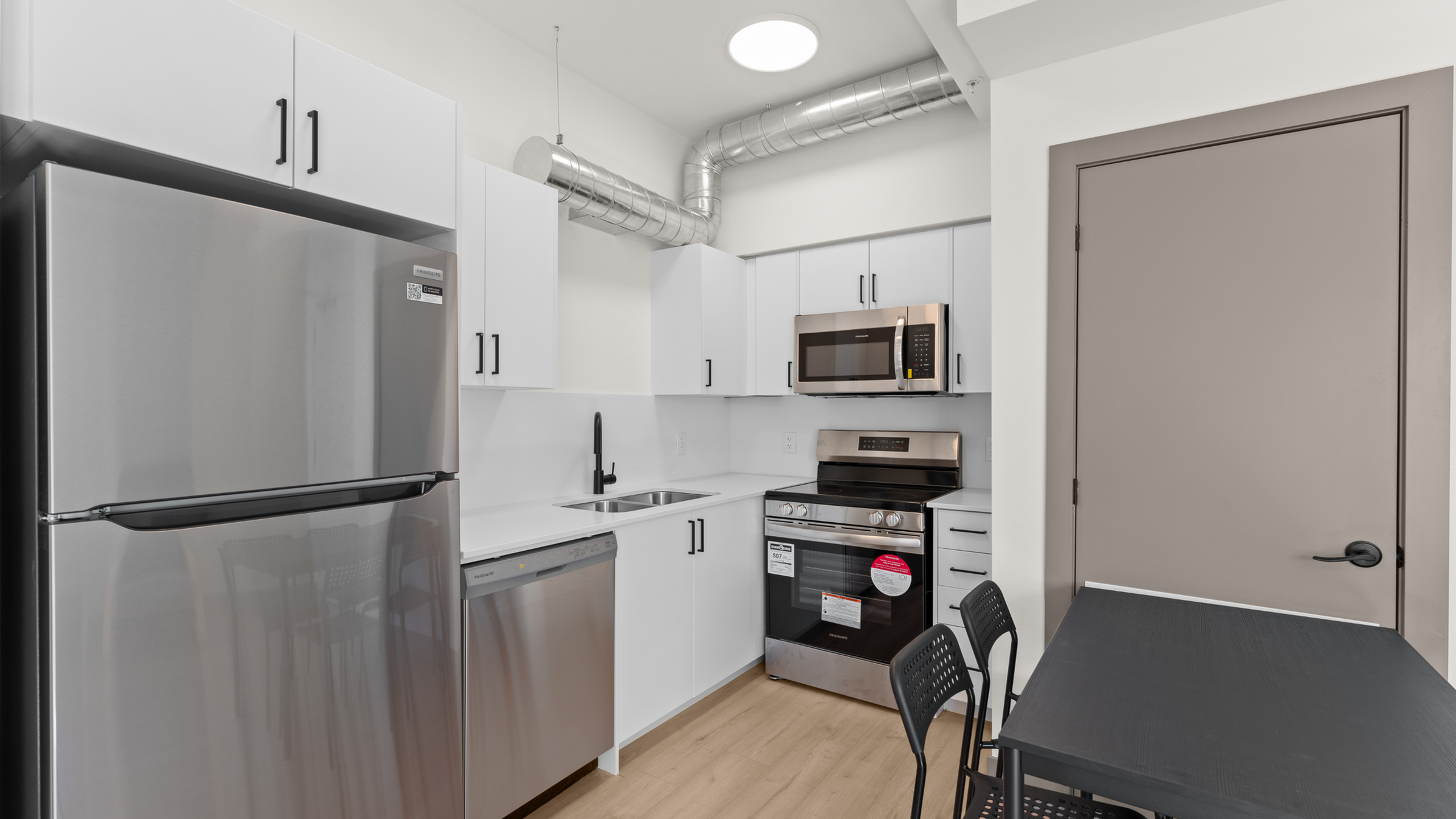 Modern kitchen with stainless steel appliances, sleek white cabinetry, and a compact dining area.