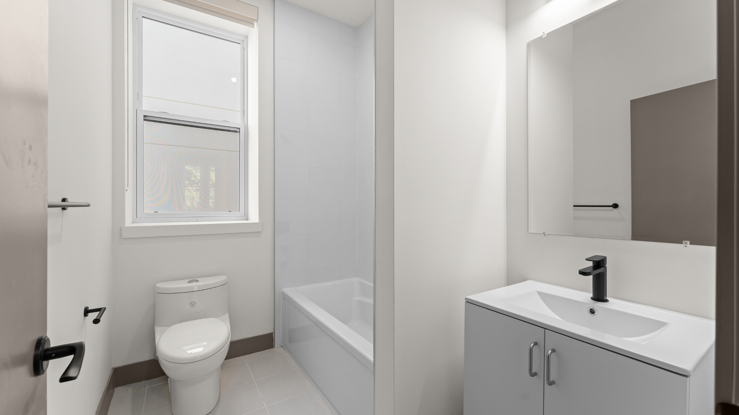 Bright and modern bathroom with sleek fixtures, featuring a bathtub, toilet, and stylish vanity mirror.