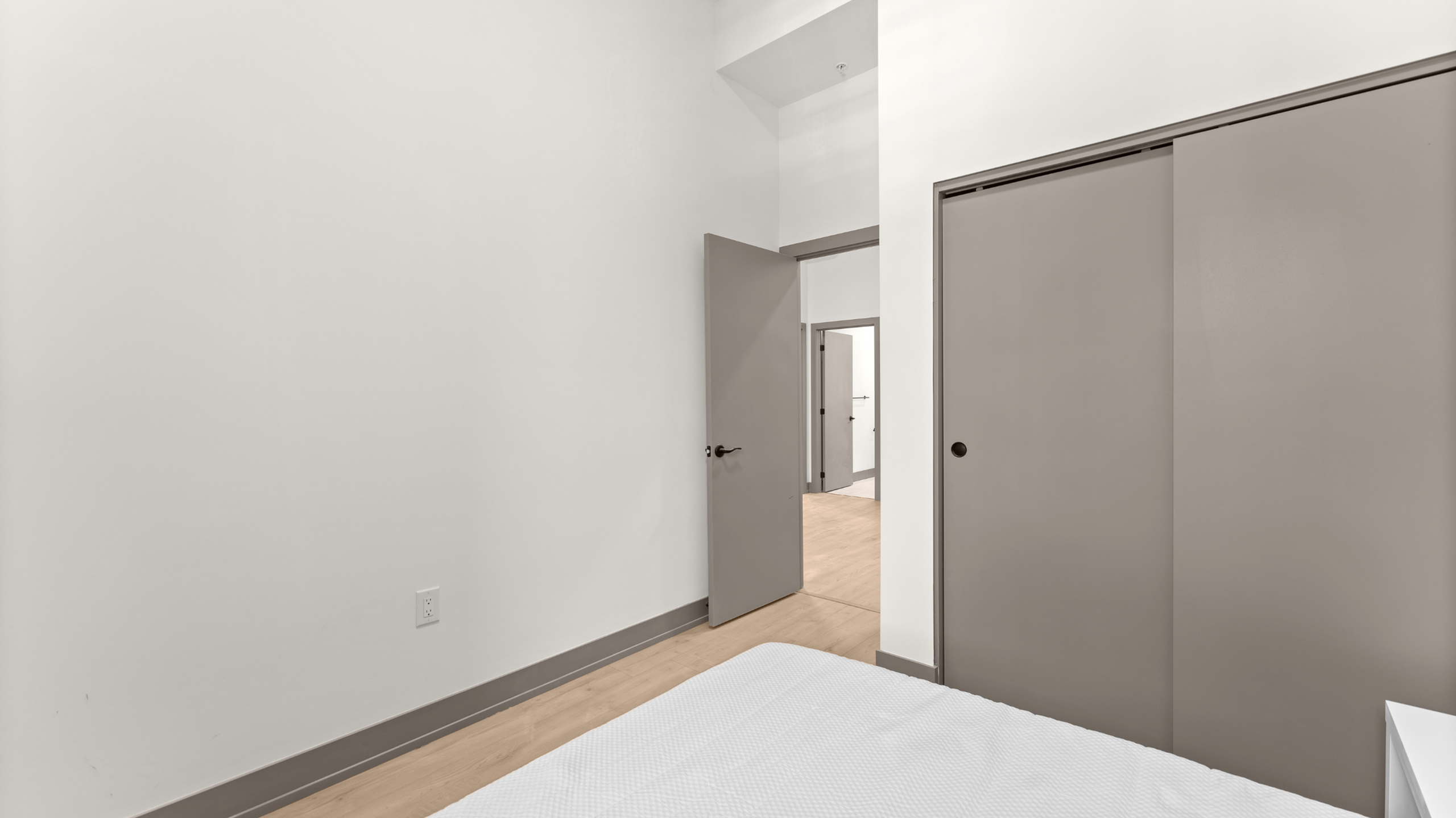 Bright, minimalist bedroom with sleek sliding closet doors and modern wooden flooring.