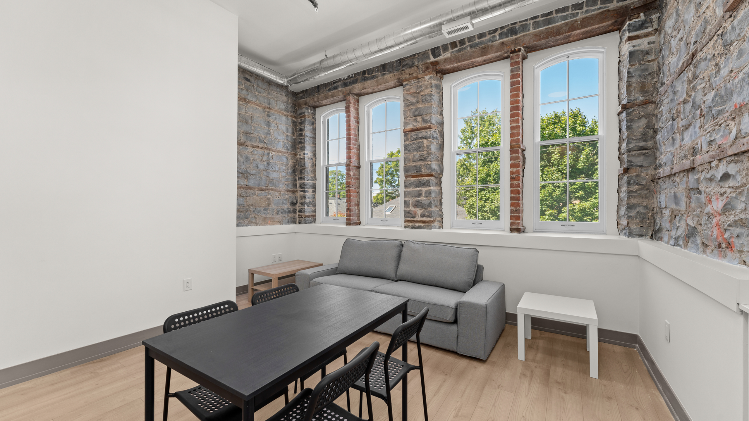 Charming living area with exposed brick walls, large windows, and modern furnishings offering a cozy and bright ambiance.