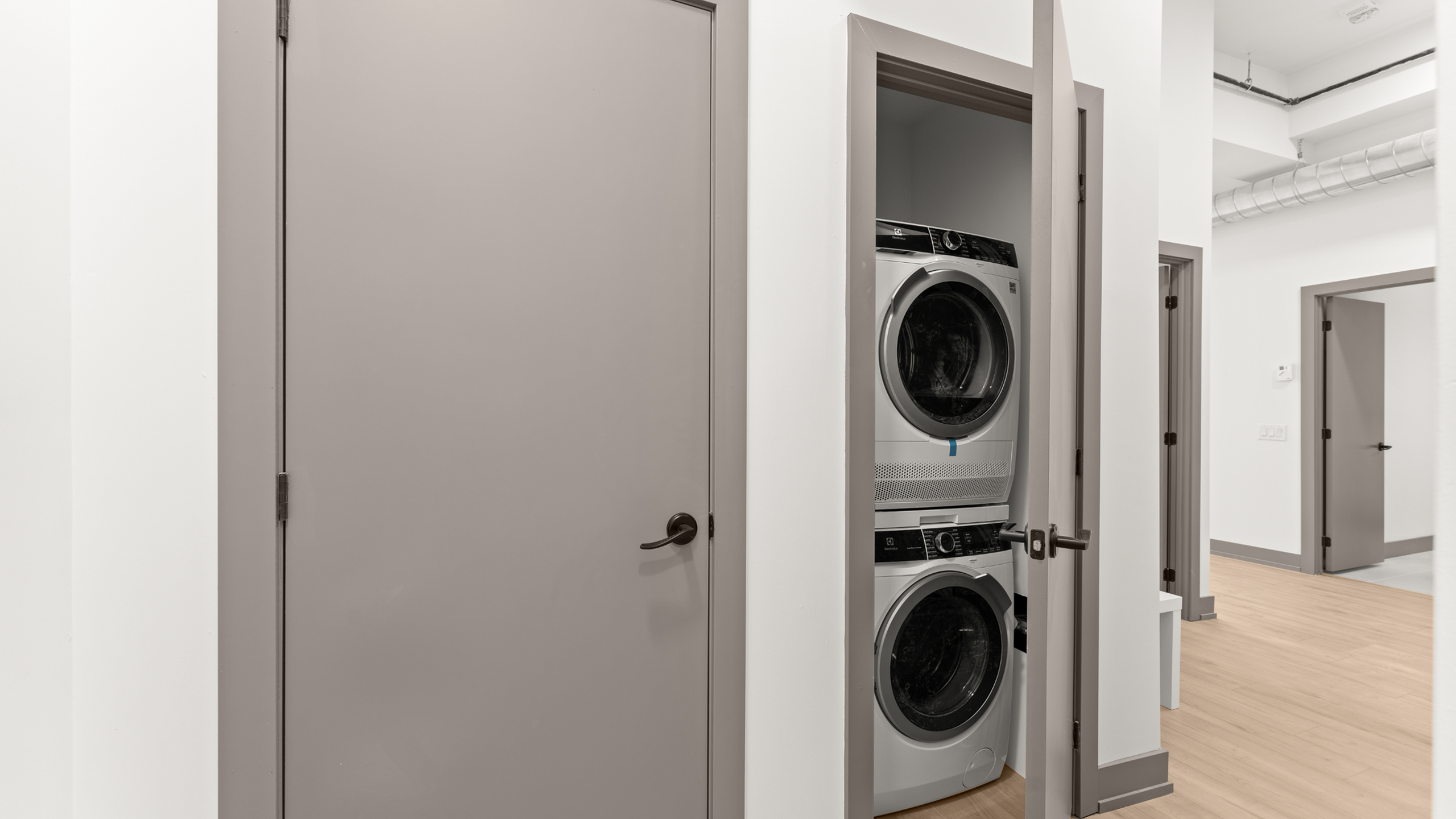 Modern apartment interior featuring an in-unit stacked washer and dryer in a sleek laundry closet.