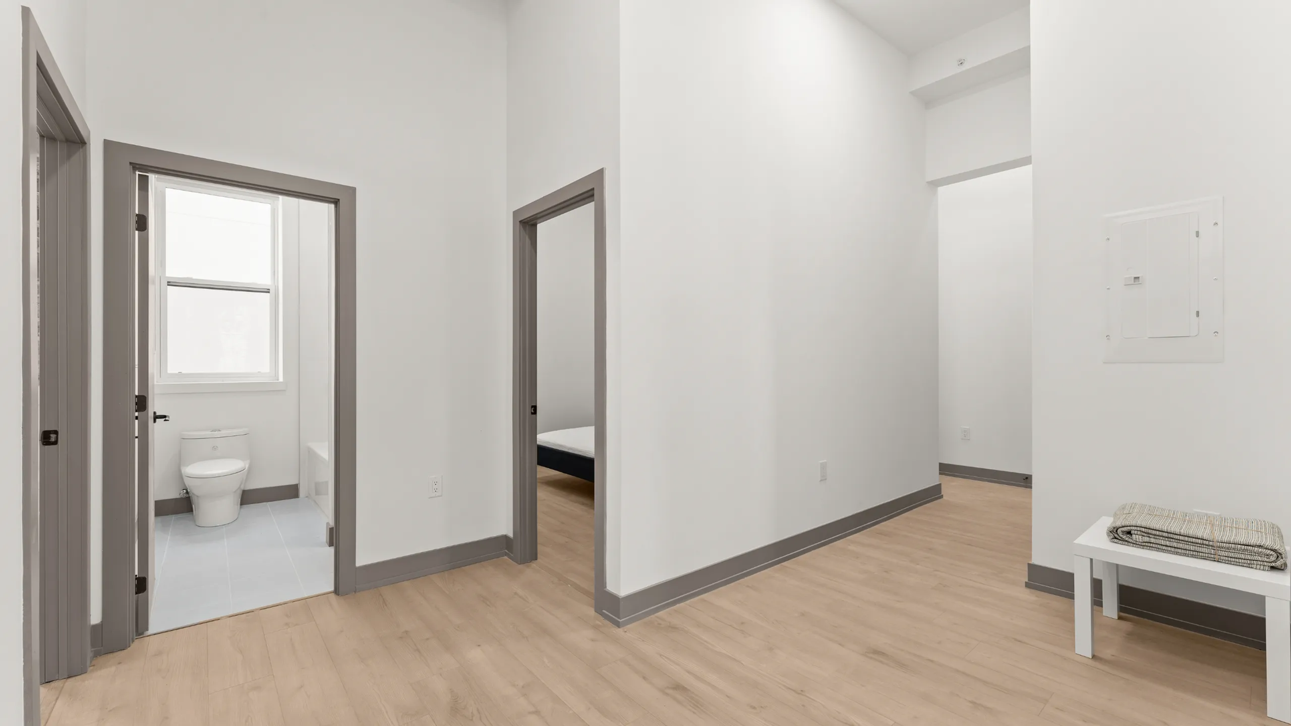 Modern apartment interior showcasing a sleek and minimal hallway with hardwood floors, leading to a bright bathroom and cozy bedroom.