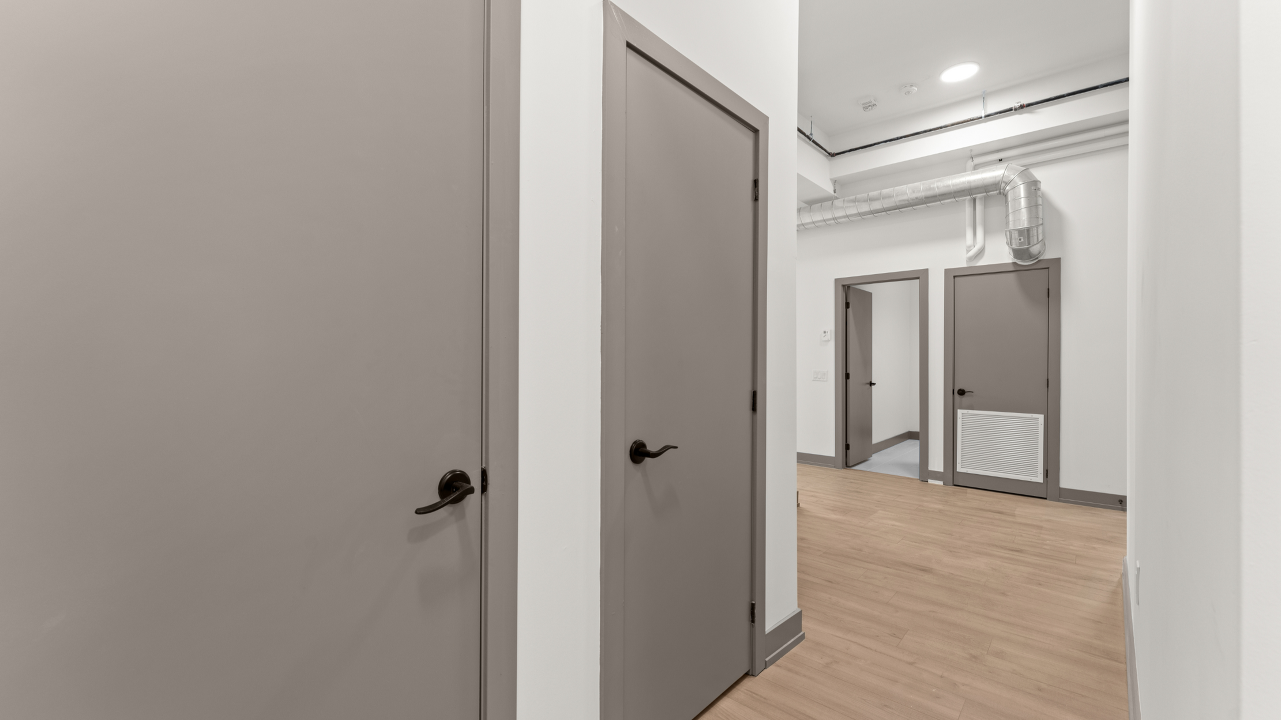 Contemporary apartment hallway with sleek wooden flooring and modern gray doors, exuding a chic and minimalist design.