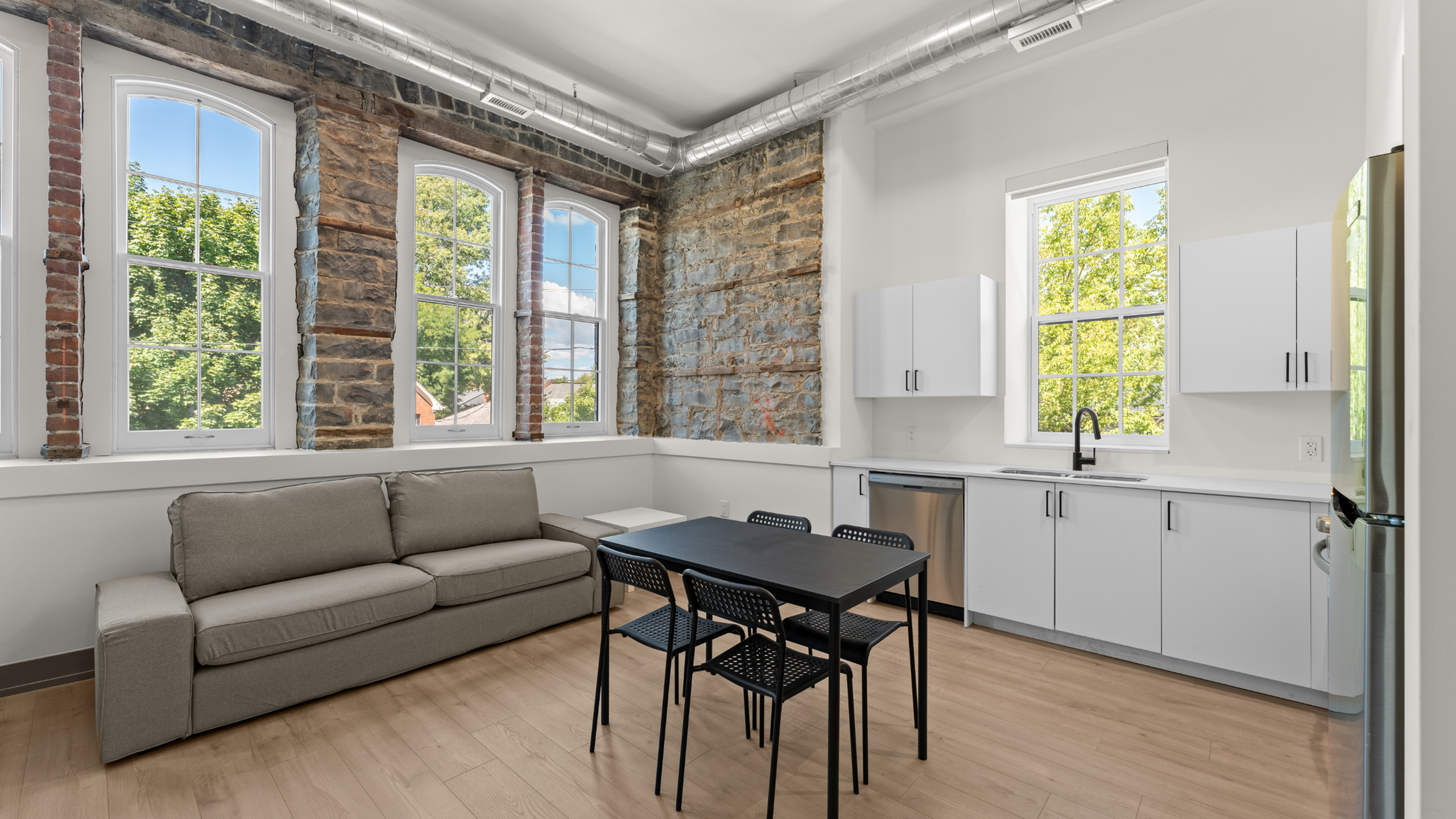 Stylish apartment living area featuring a cozy sofa, modern dining set, and a sleek kitchen with large windows and exposed brick accents.