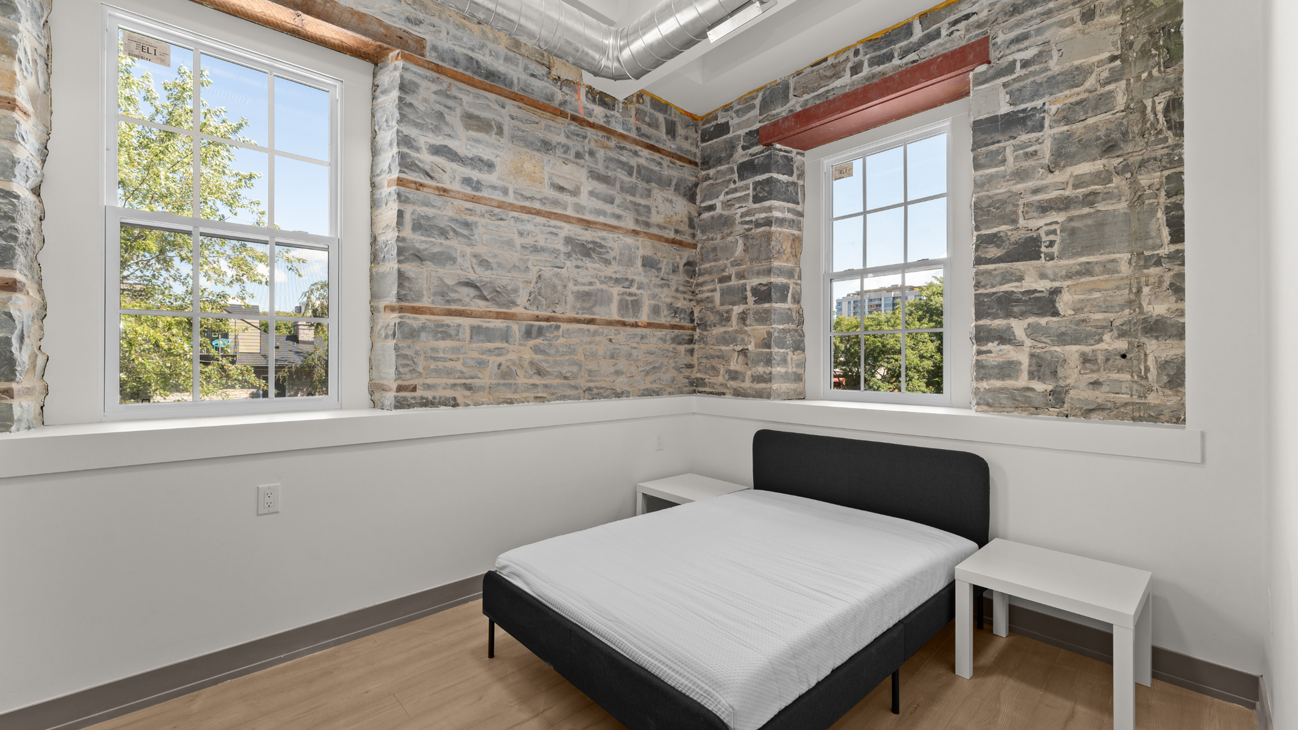 Charming bedroom with a rustic stone accent wall and large windows, offering natural light and a cozy atmosphere.