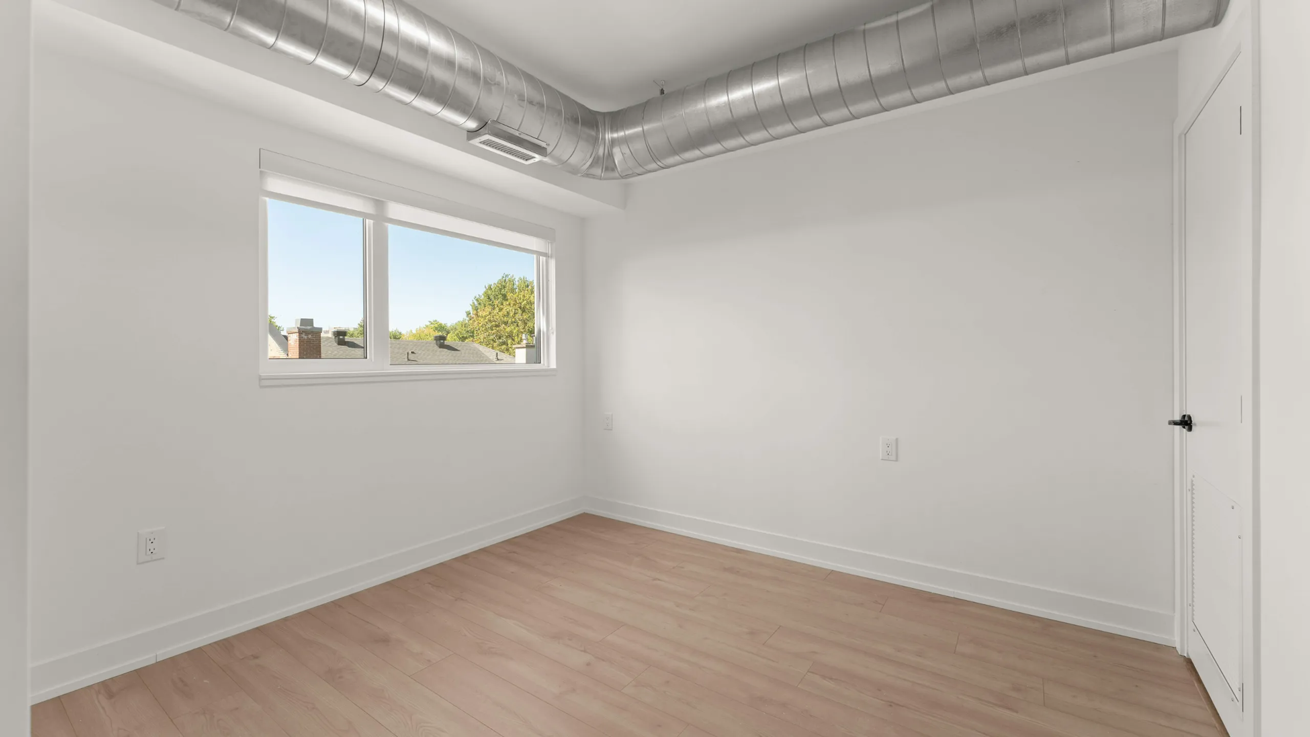 Bright room with modern hardwood floors and large window, featuring stylish exposed ductwork.