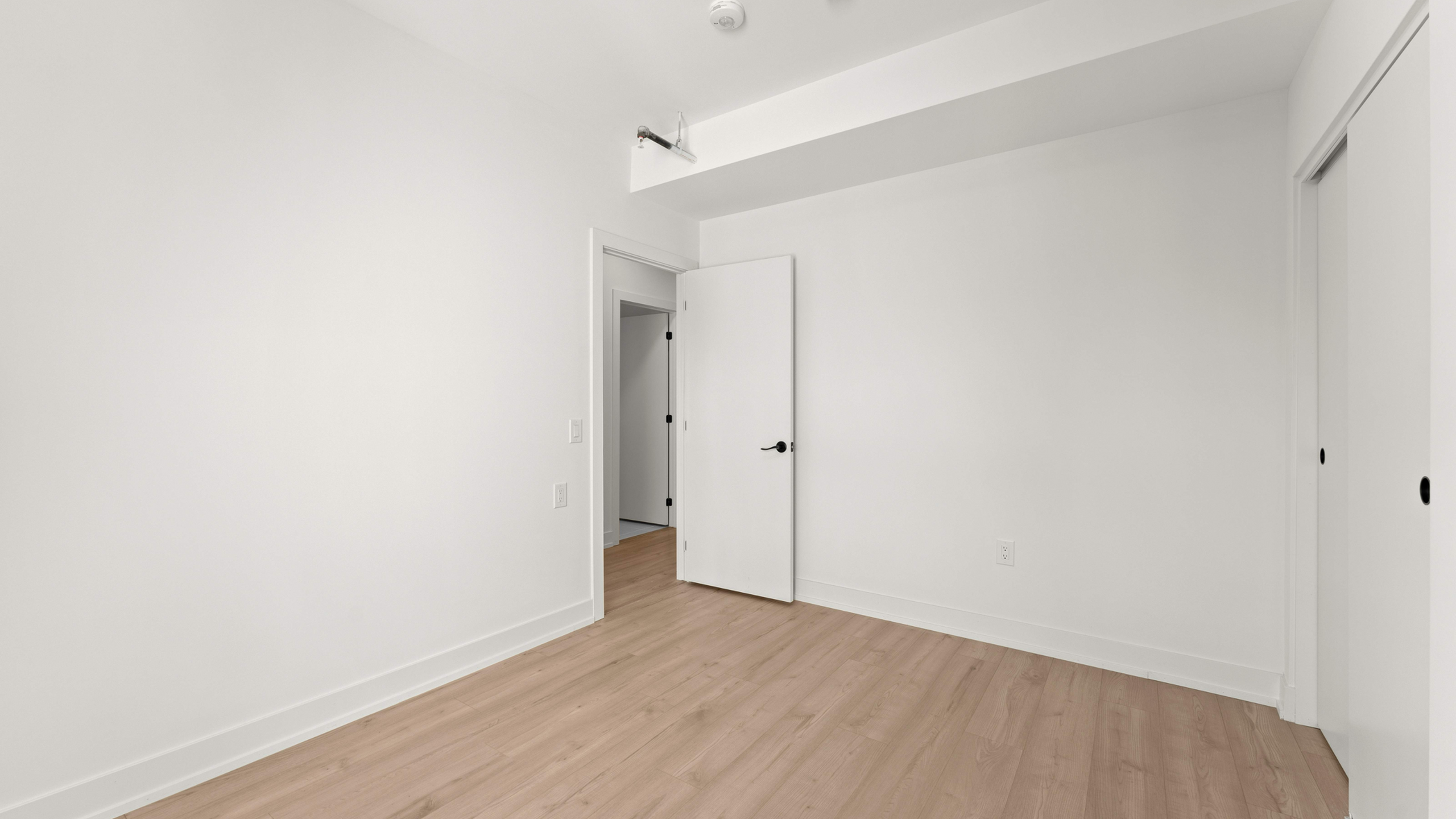 Bright, spacious empty room with sleek wooden flooring and modern white walls, ideal for customization.