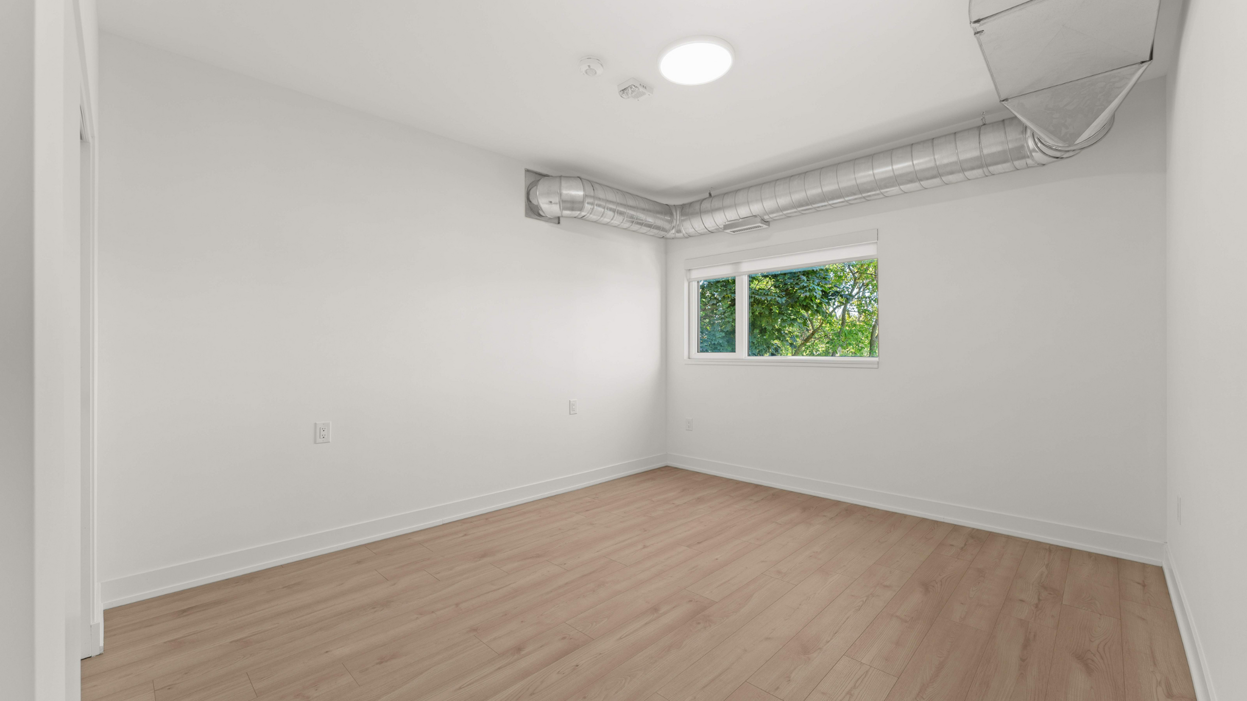 Bright, spacious room with modern ductwork and large window offering a serene view, perfect for a home office or cozy bedroom.