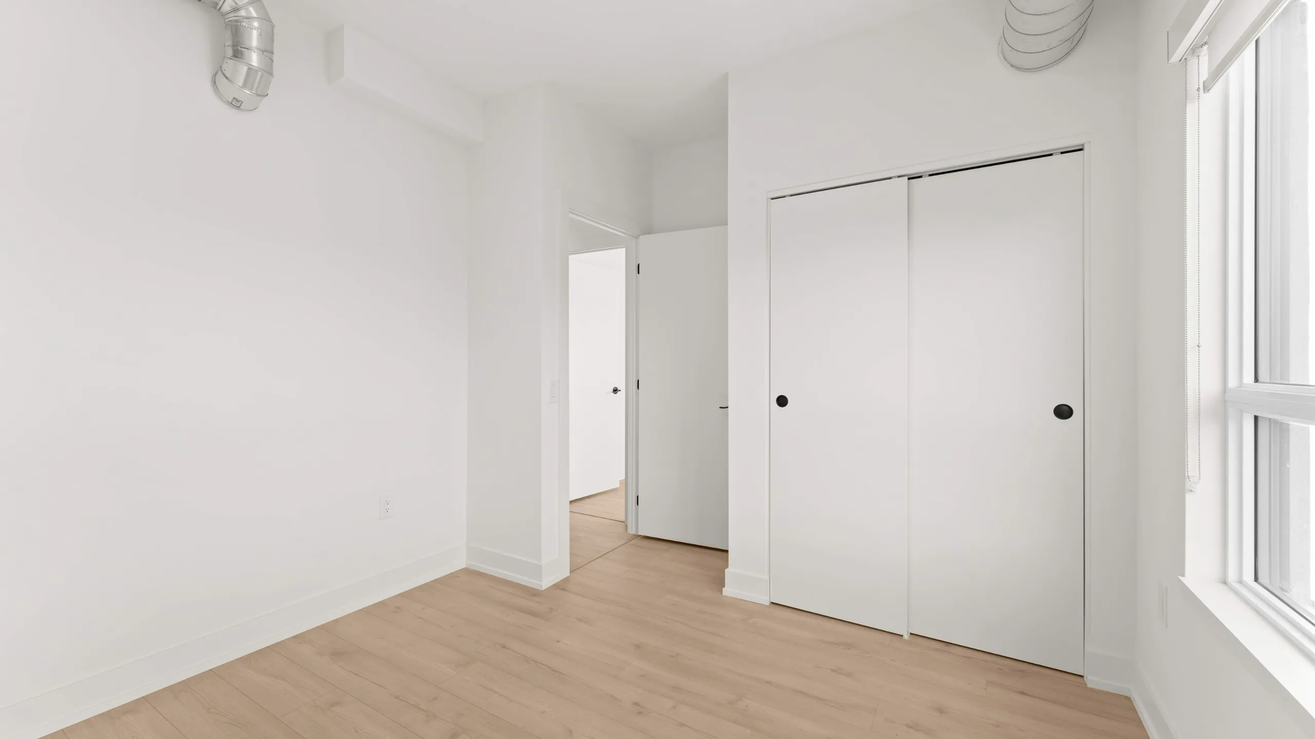 Bright room with sleek hardwood flooring, large window, and modern closet doors, ideal for a cozy bedroom or stylish office space.
