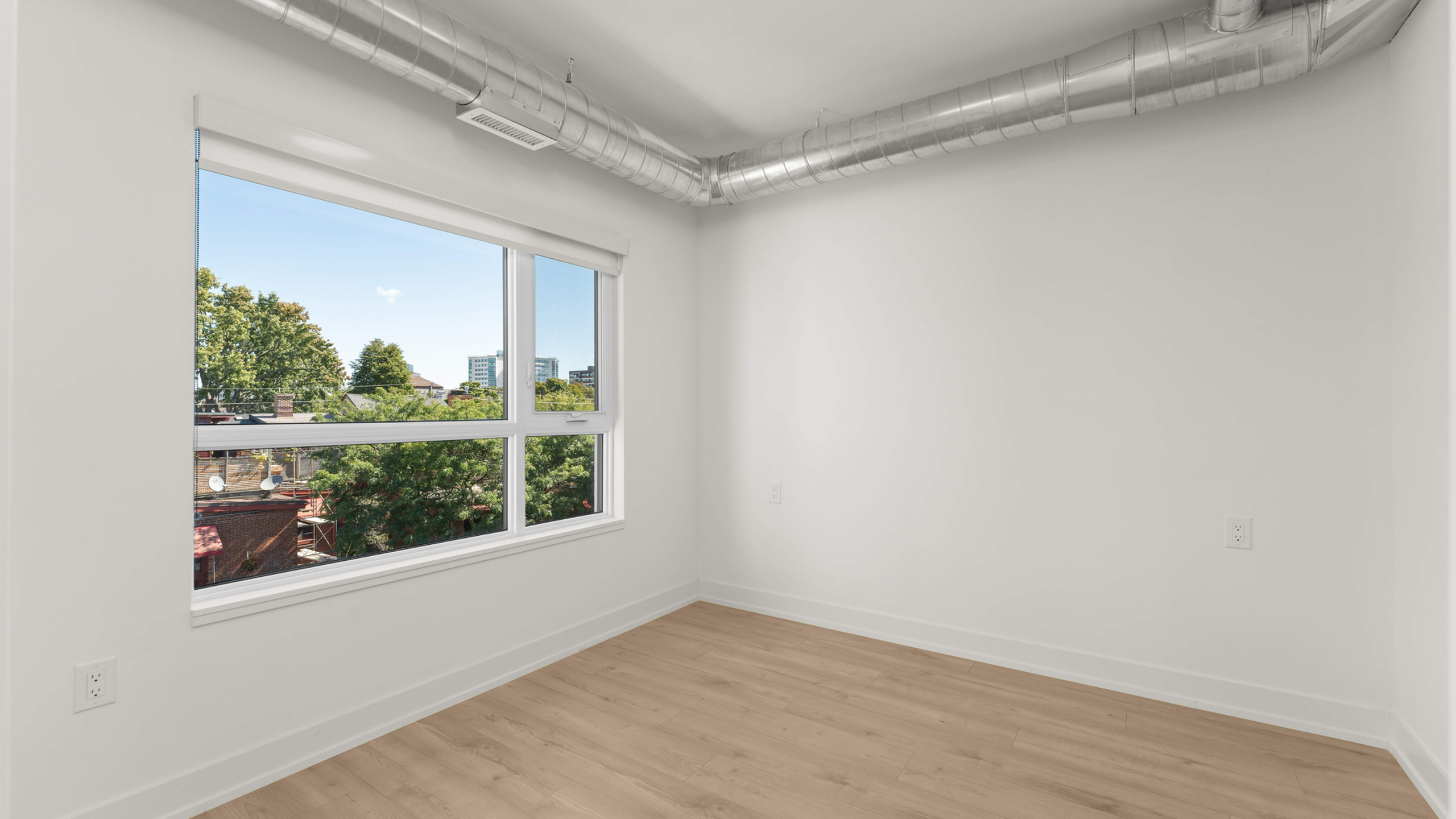 Bright room with wide window offering a beautiful cityscape view, featuring sleek hardwood floors and modern exposed ductwork.