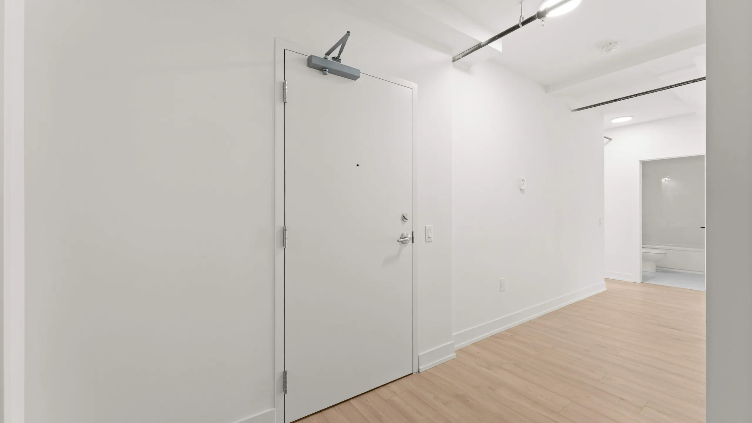 Modern apartment entryway featuring sleek white walls, warm hardwood flooring, and a minimalist door design.