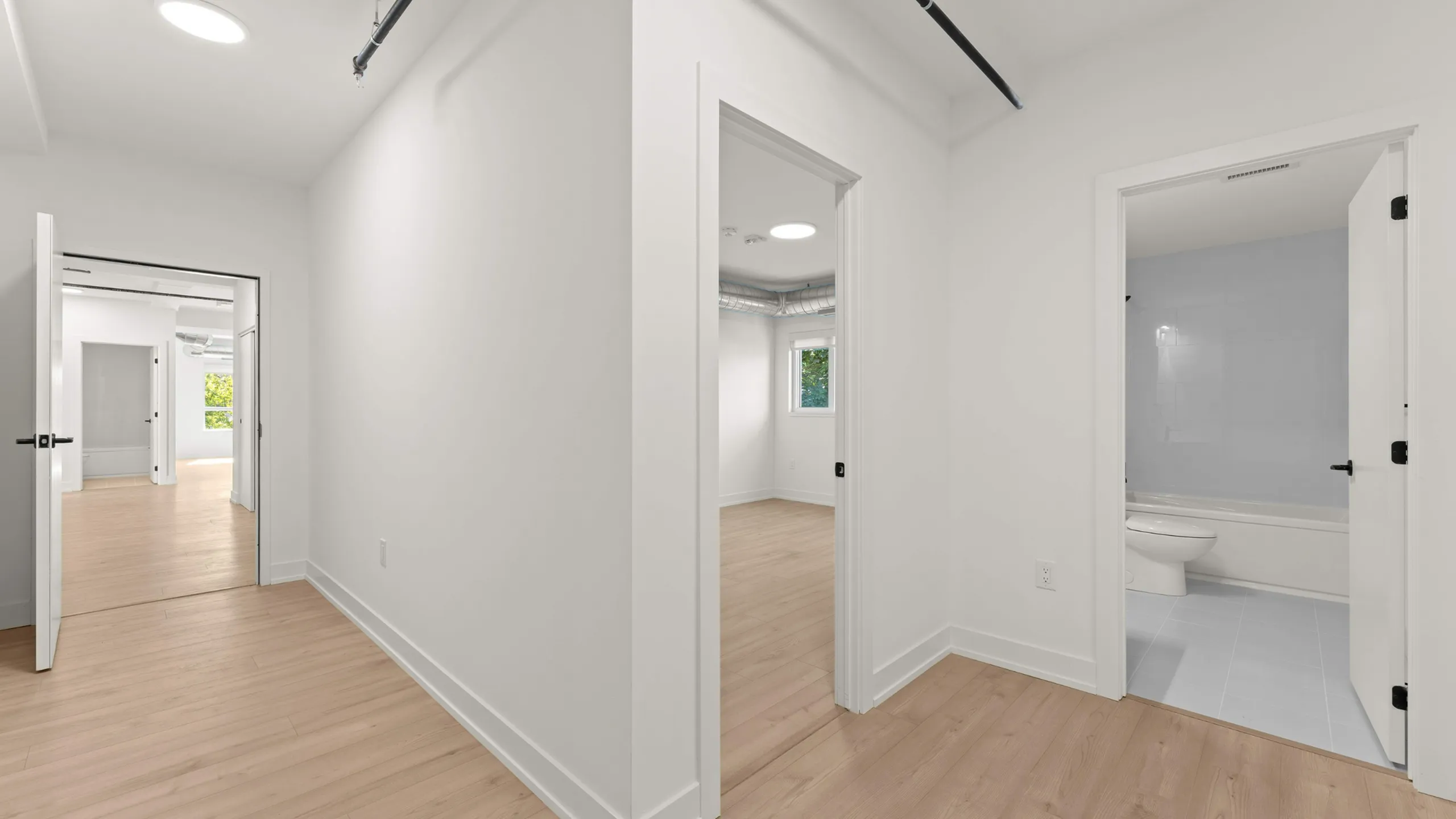 Bright hallway with modern light fixtures leading to a spacious living area and a stylish bathroom. Natural wood flooring enhances the elegance of the space.