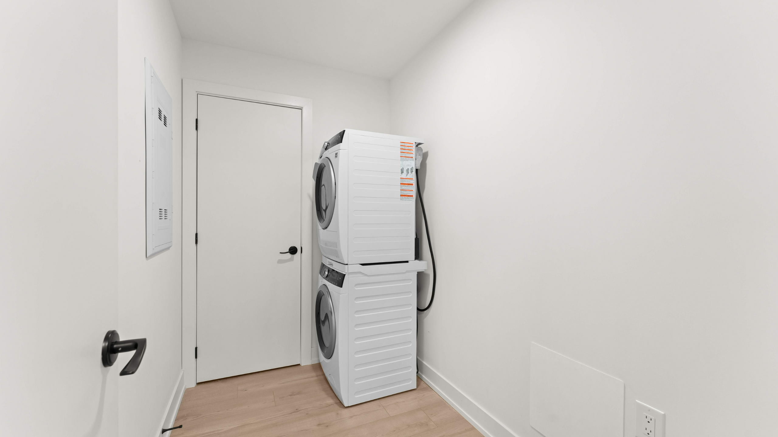 Modern laundry room with stacked washer and dryer against a sleek white wall, featuring elegant wooden flooring.