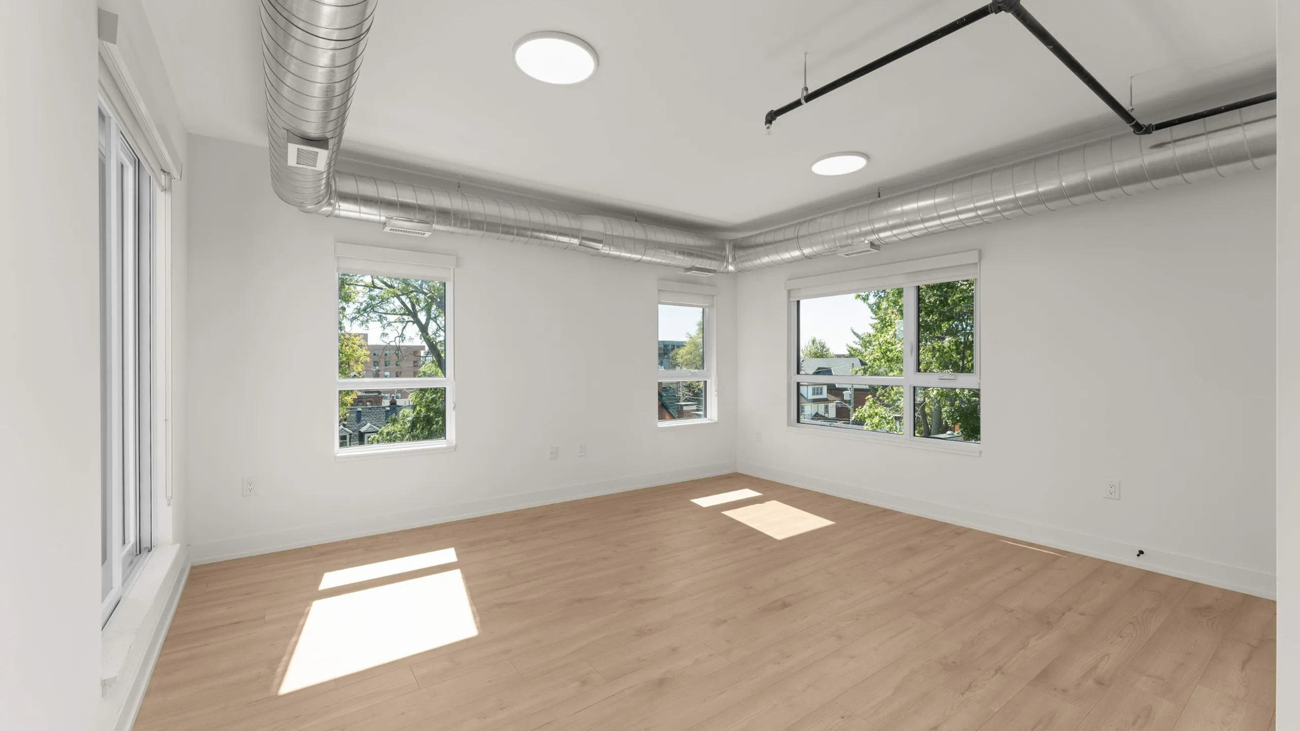 Bright and airy room with large windows, sleek wooden flooring, and industrial exposed ductwork.