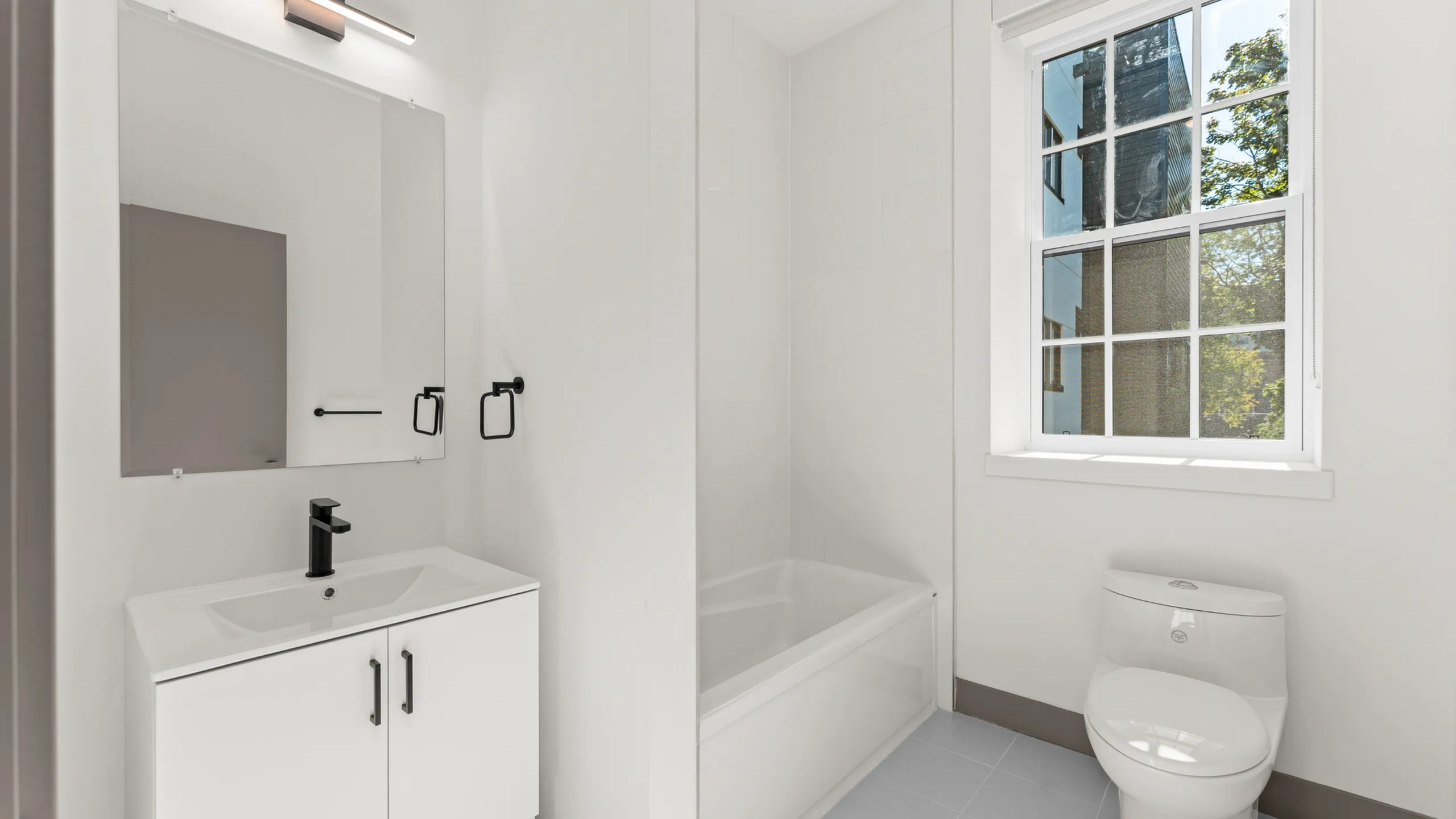 Bright and modern bathroom featuring a sleek white vanity, stylish black fixtures, and a sunlit window.