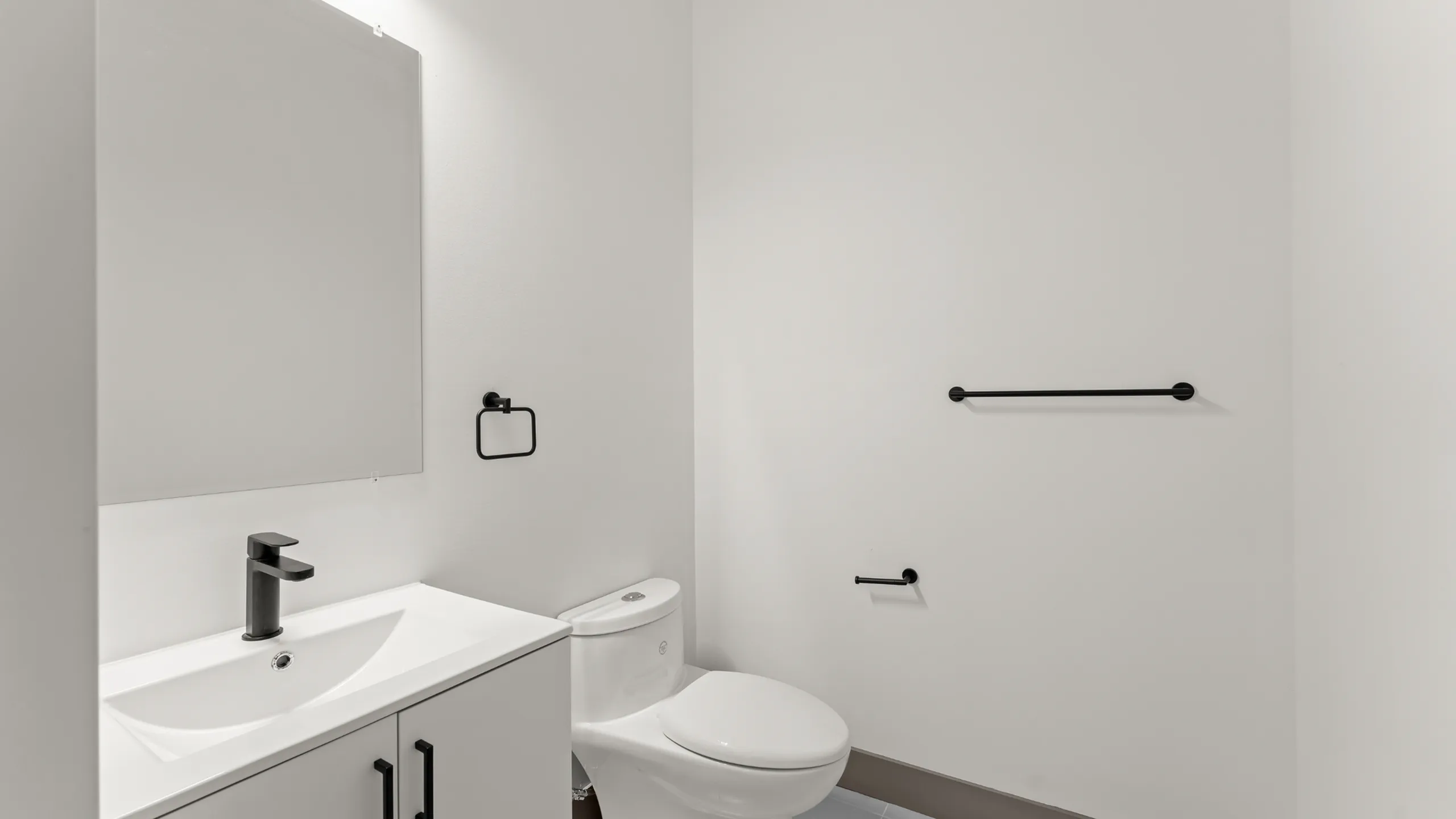 Modern minimalist bathroom with sleek fixtures, featuring a pristine white sink, stylish black faucet, and elegant toilet.